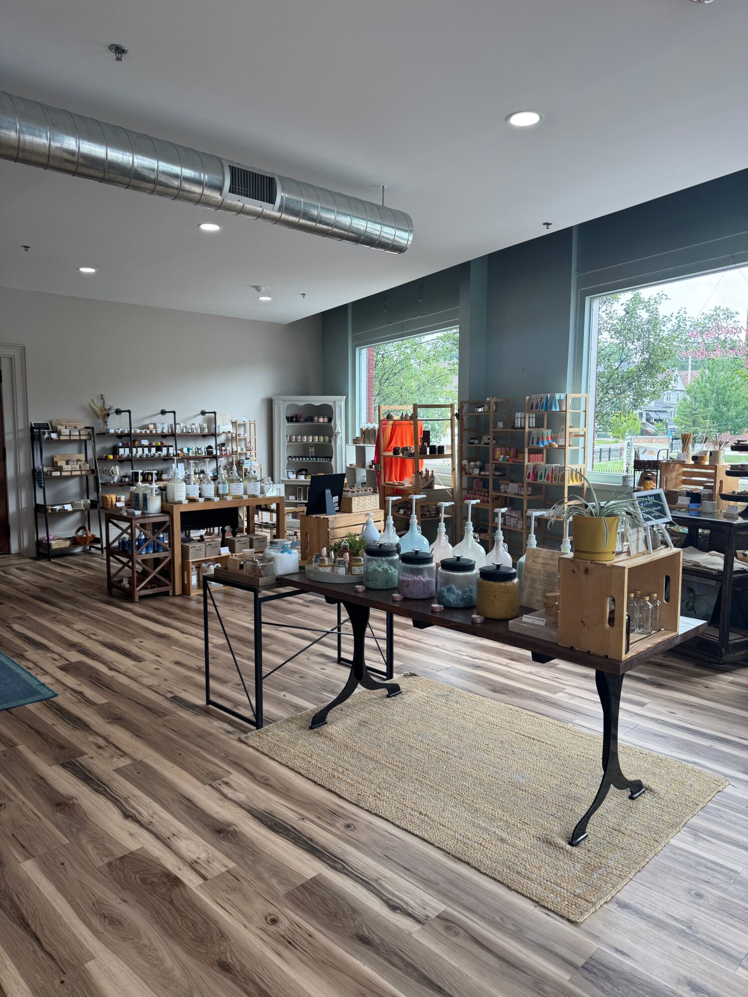 Display of various bottles and products on tables in a room with large window, wooden floor, and natural light.