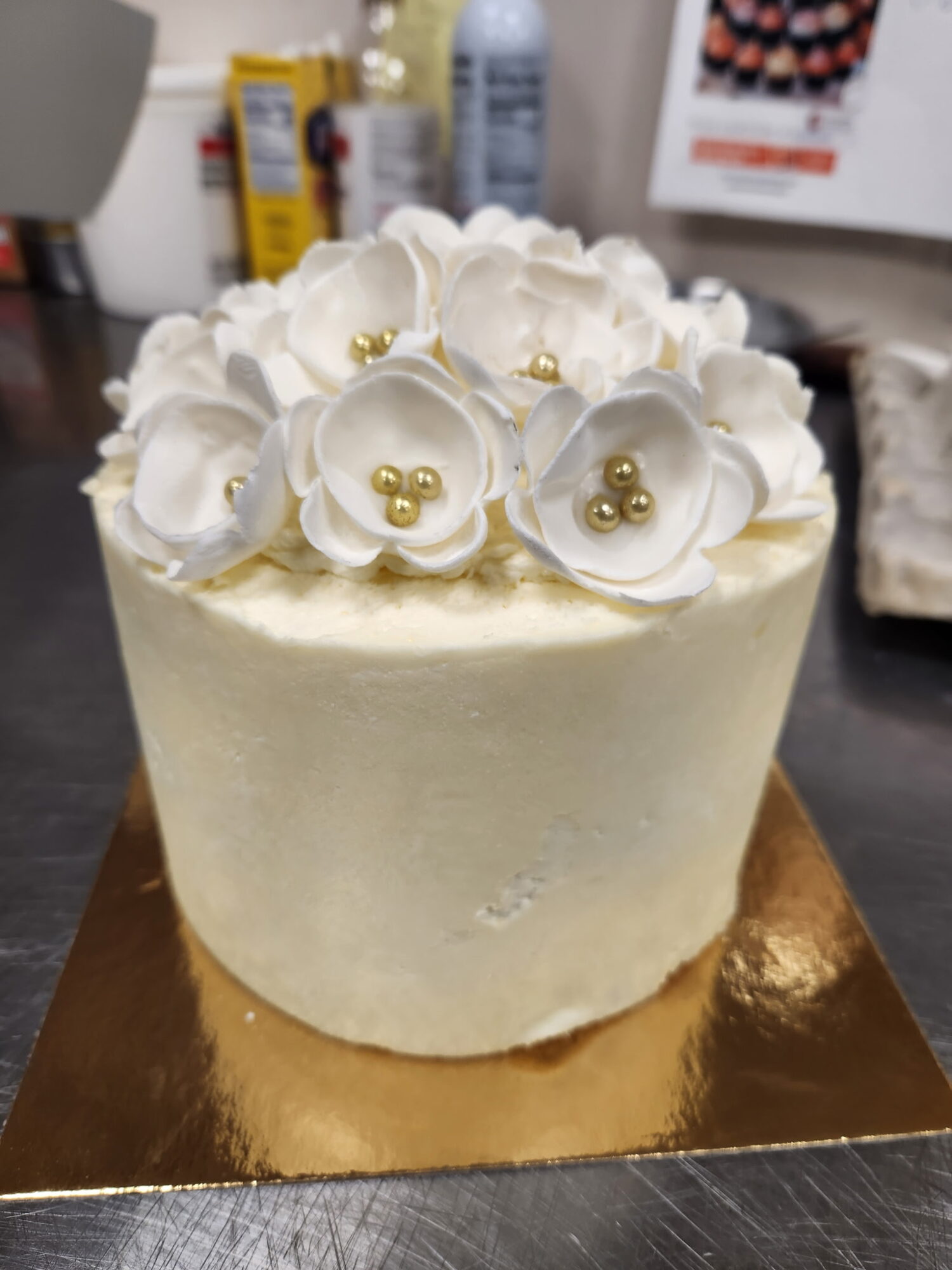 White cake with white flower decorations and gold beads on top, on a gold-colored base.