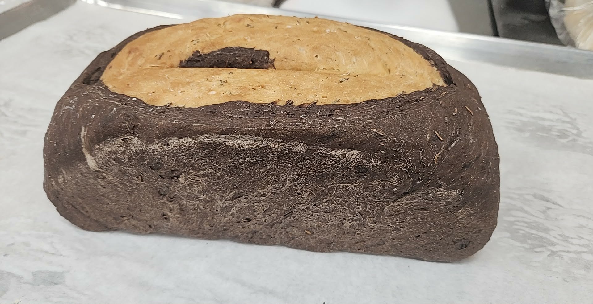 A loaf of bread with a dark crust and a light, soft interior, resting on white paper.