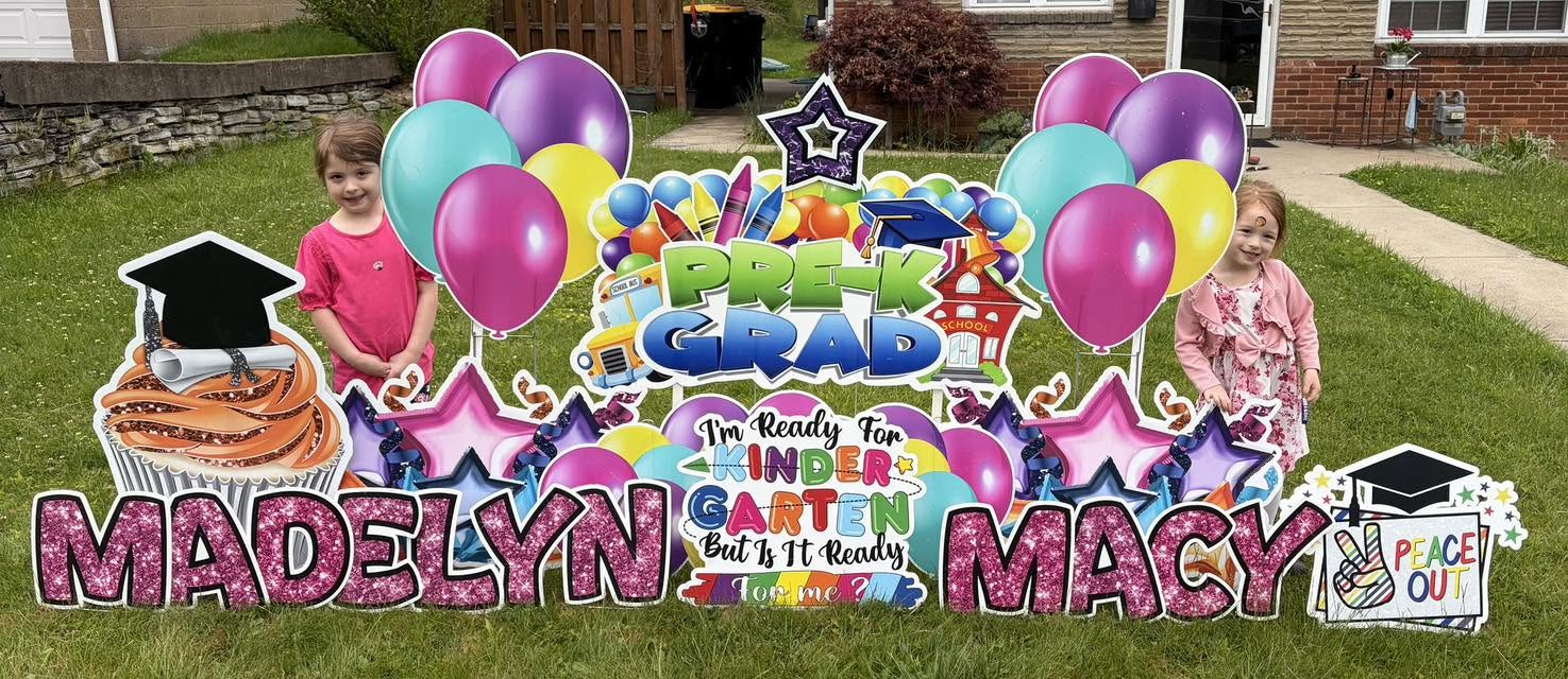 Colorful birthday yard display with balloons, cake, and children's names Madelyn and Macy, celebrating a graduation.