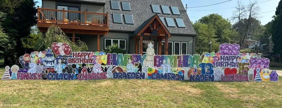 Colorful birthday signs with balloons and decorations on a lawn in front of a house.