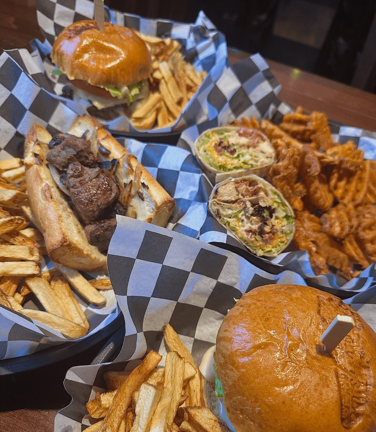 Burger with lettuce and fries, half-cut burger with meat and toppings, fried chicken pieces, and a sandwich with fries on checkered paper