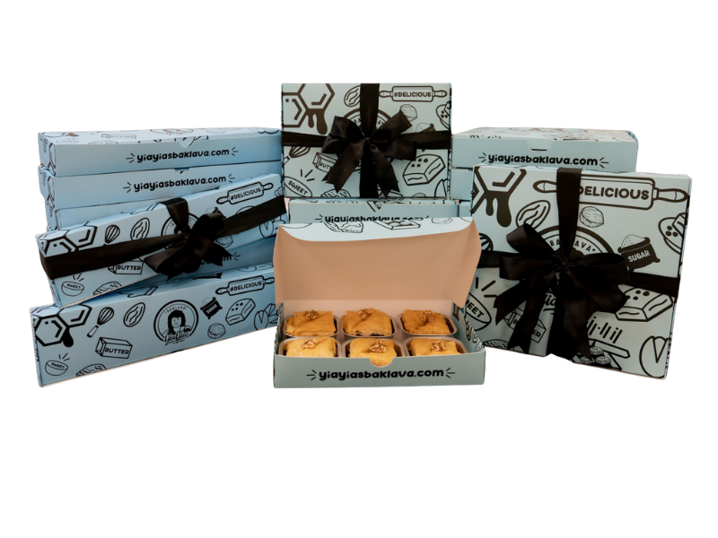 Open box with cookies, surrounded by stacked boxes with black ribbons, black and white designs, and website URL. Black background.