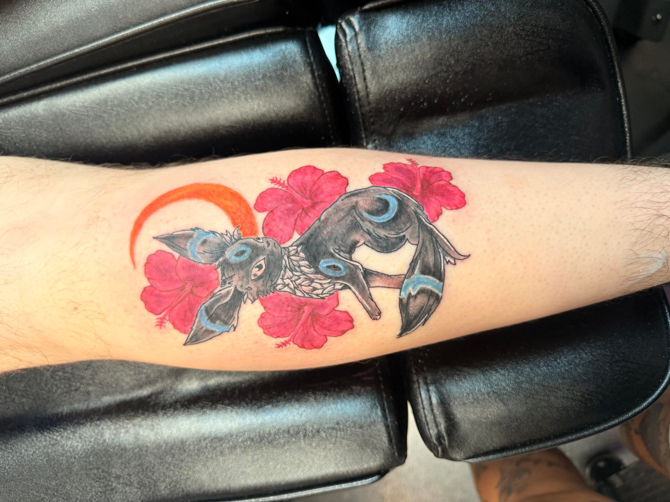 Tattoo of a bird with colorful feathers surrounded by red flowers on a person's arm.