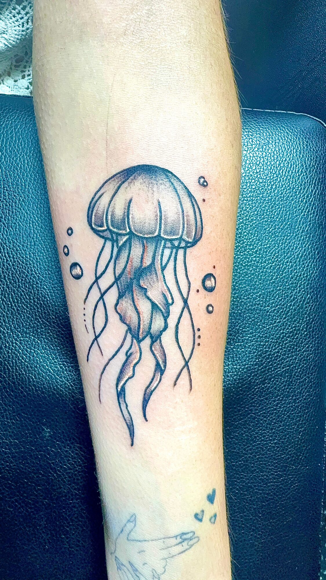 Tattoo of a jellyfish with flowing tentacles, surrounded by small bubbles on a person's arm.