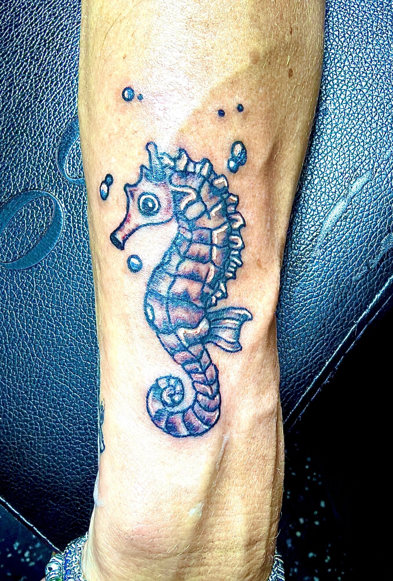 Seahorse tattoo with bubbles on person's arm, detailed with blue shading and line work.