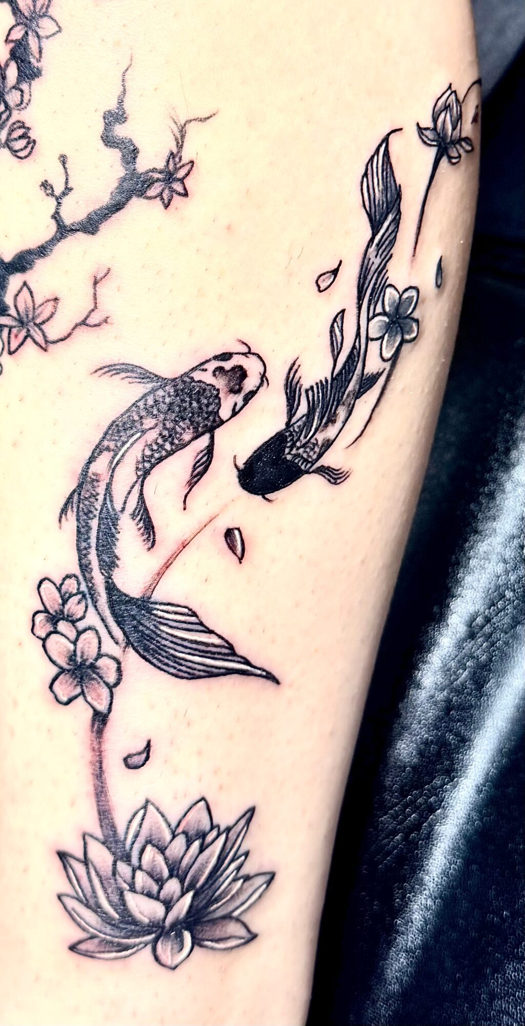 Tattoo of two koi fish swimming among flowers and a lotus flower at the bottom.
