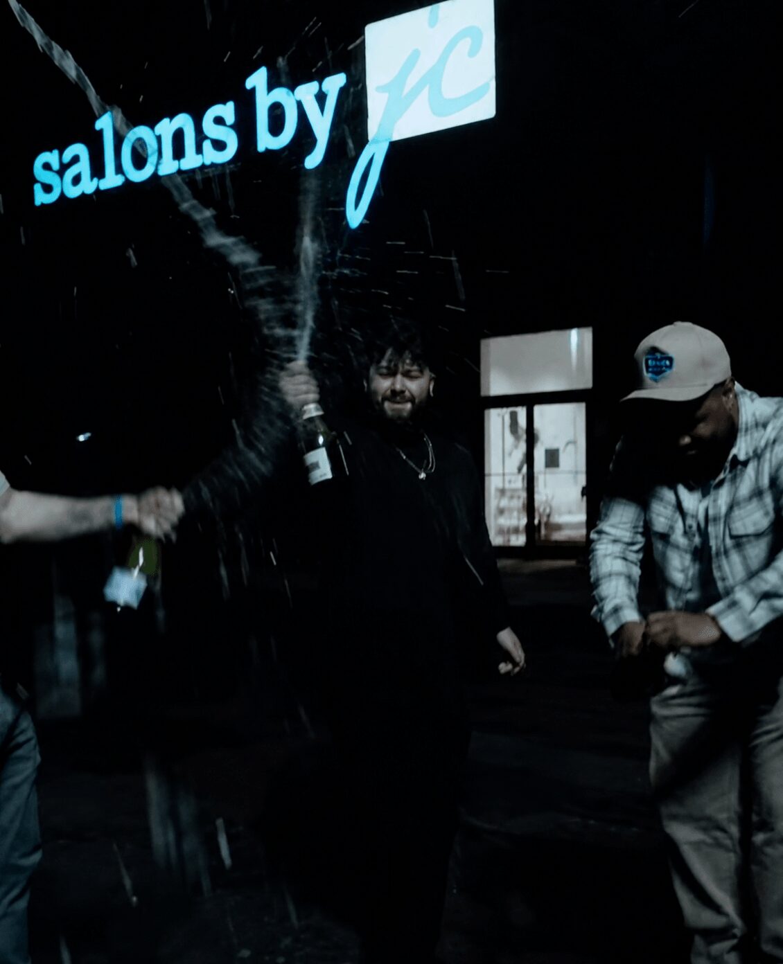 People celebrating with drinks in front of a sign that reads 'salons by jc'.