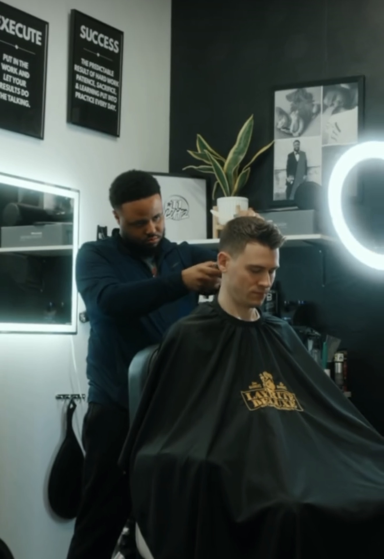 Barber cutting young man's hair in a modern salon with framed pictures and plants on the wall.