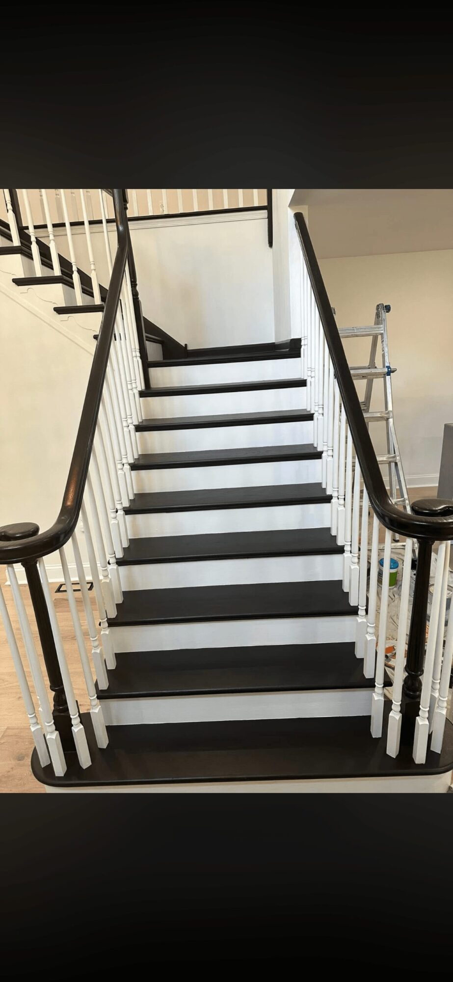 Black and white staircase with wooden handrails and white spindles, leading upward indoors.