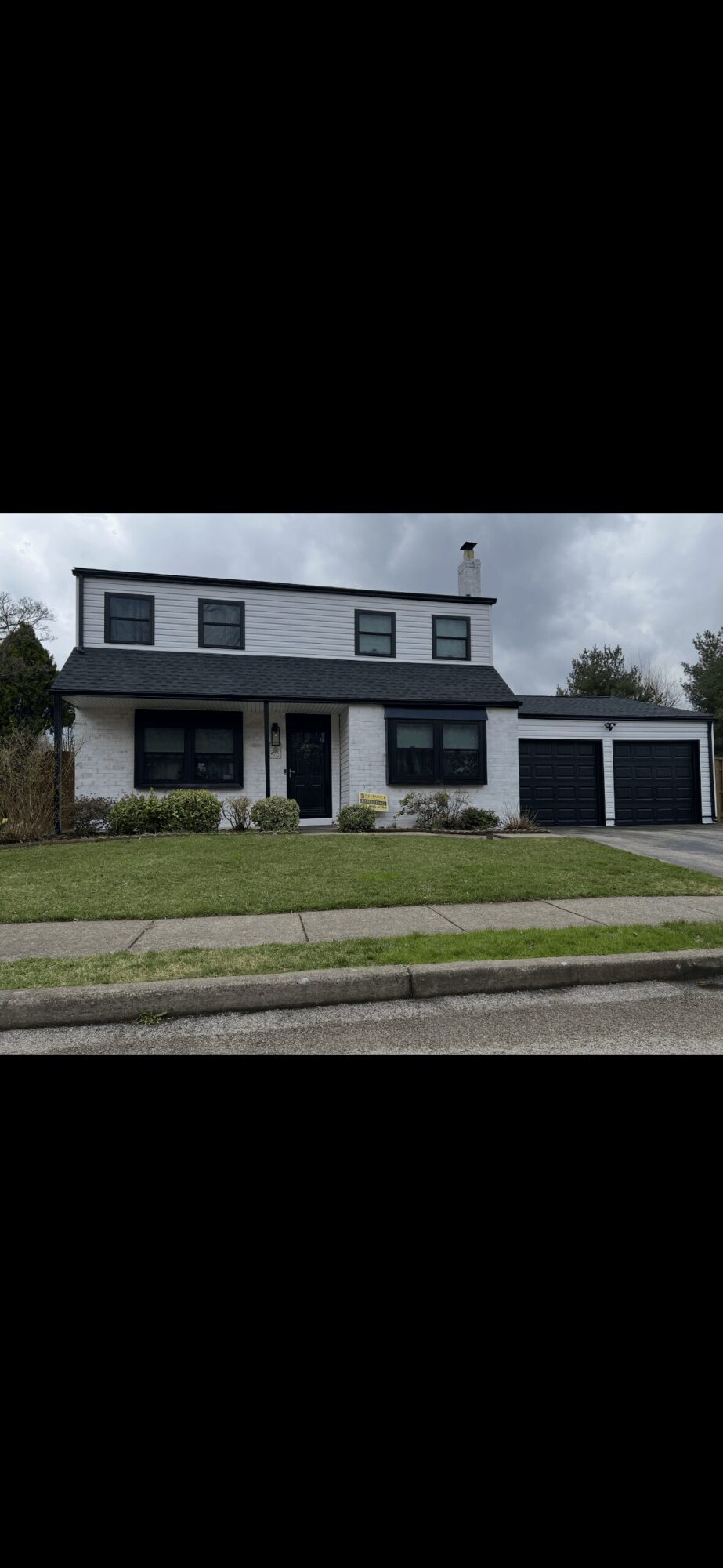 Two-story house with a garage, front lawn, and sidewalk, under a cloudy sky.