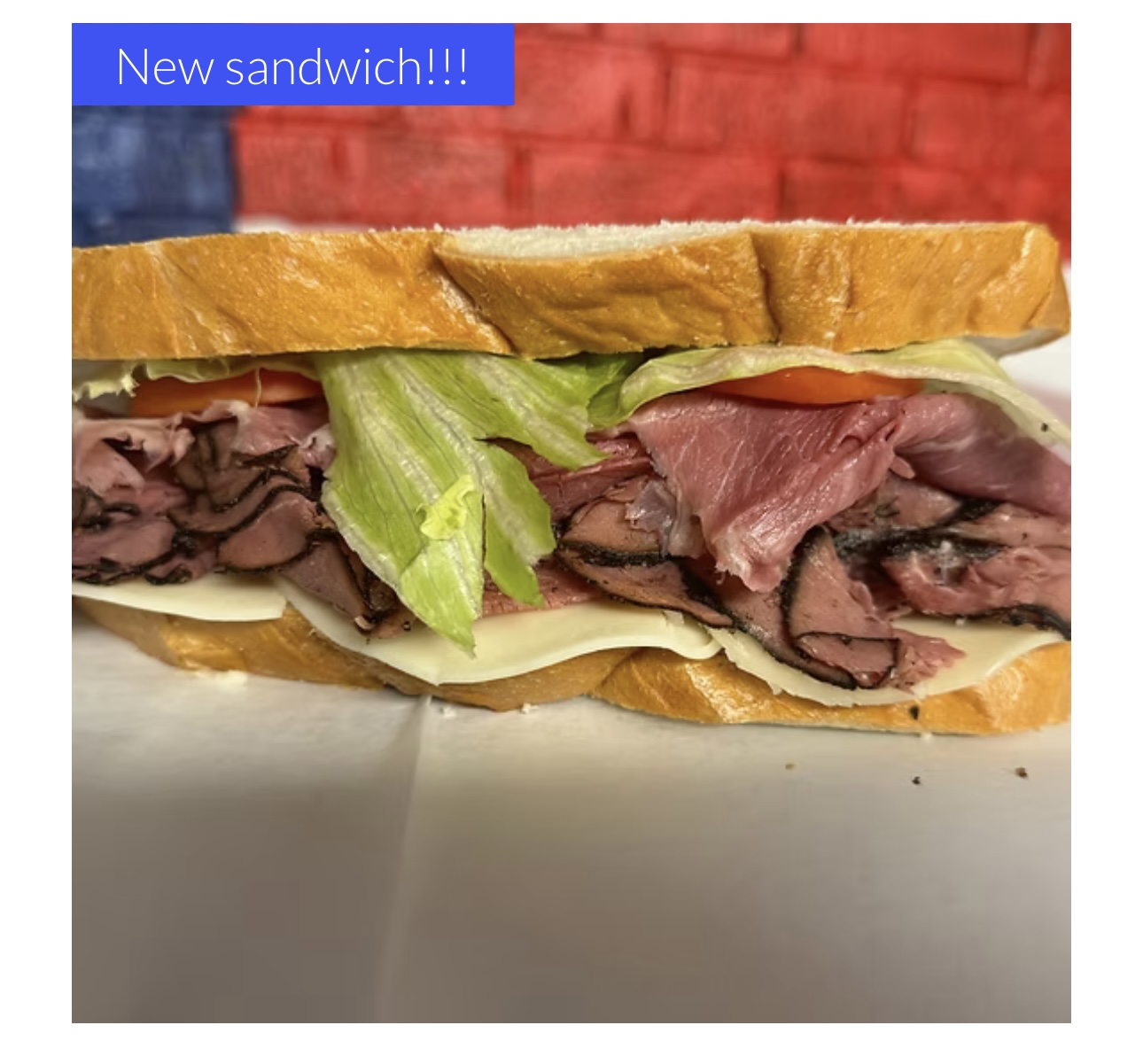 Sandwich with sliced roast beef, lettuce, tomato, and cheese on a baguette, with a blue label saying 