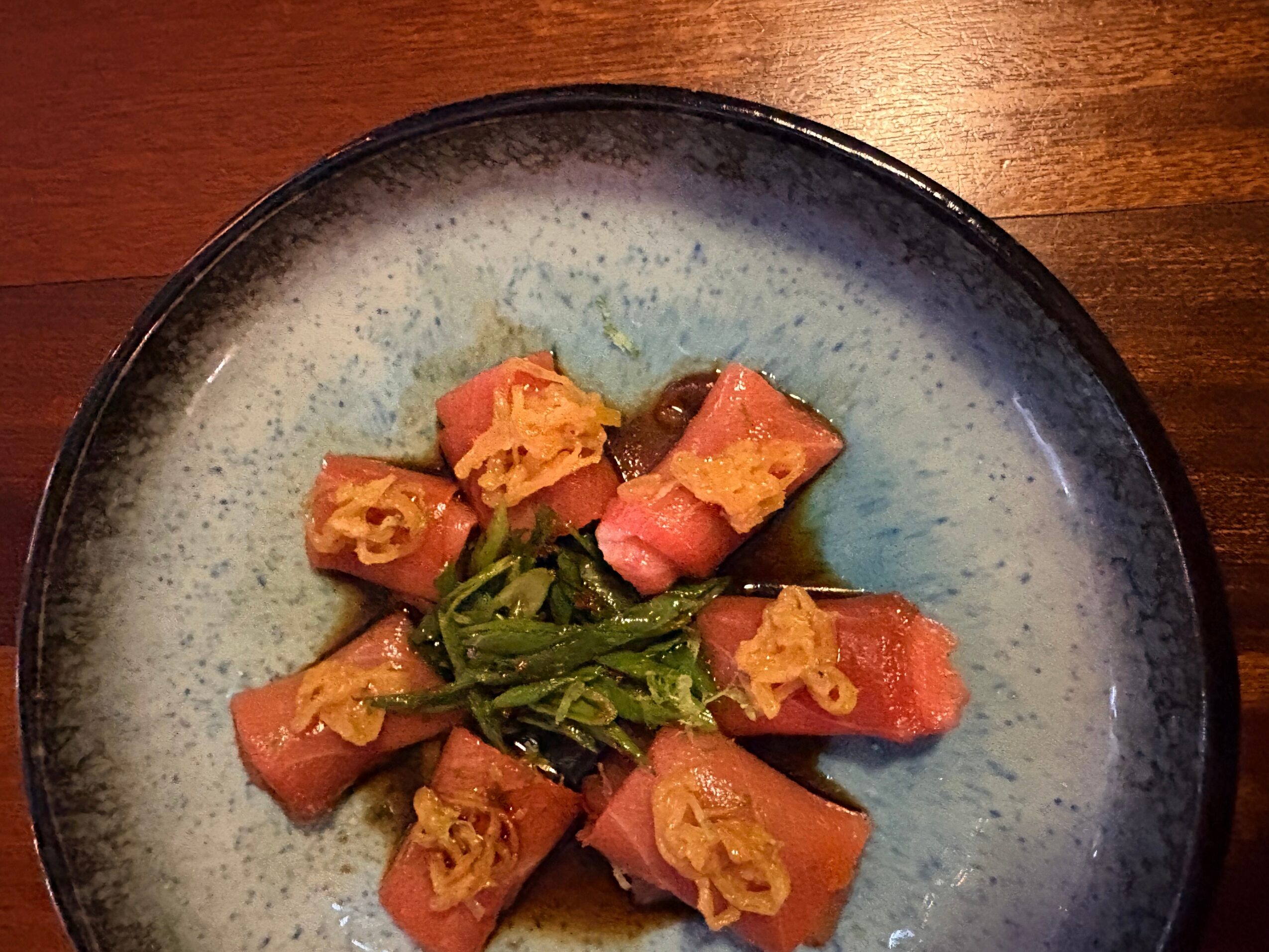 A plate with sliced pink and orange food, garnished with green herbs, on a wooden surface.