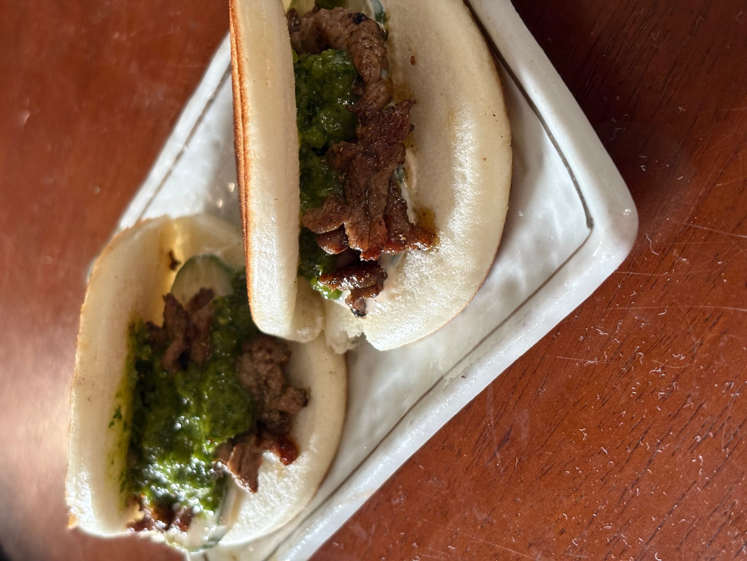 Two steamed buns filled with meat and green sauce on a white plate, viewed from the side.