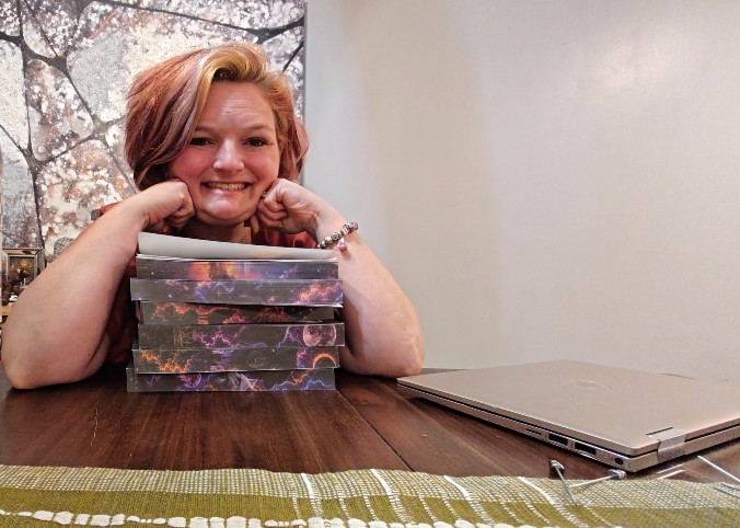 Smiling woman with short hair resting her chin on her hands, sitting at a table with a closed laptop and a decorative box.