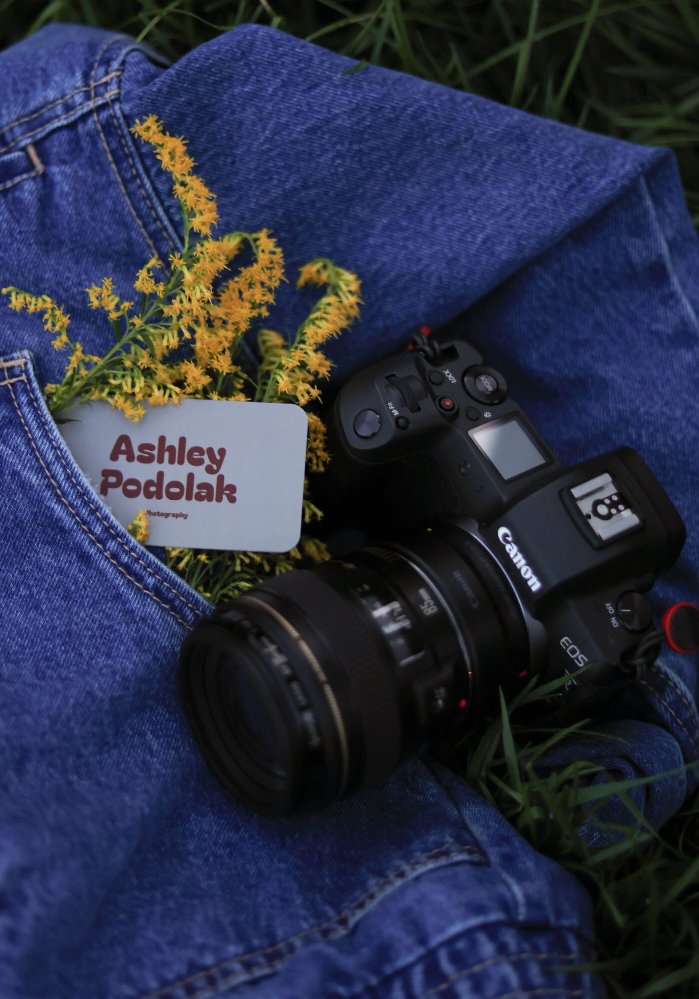 Camera, name tag, and yellow flowers on denim fabric outdoors, with grass in background.