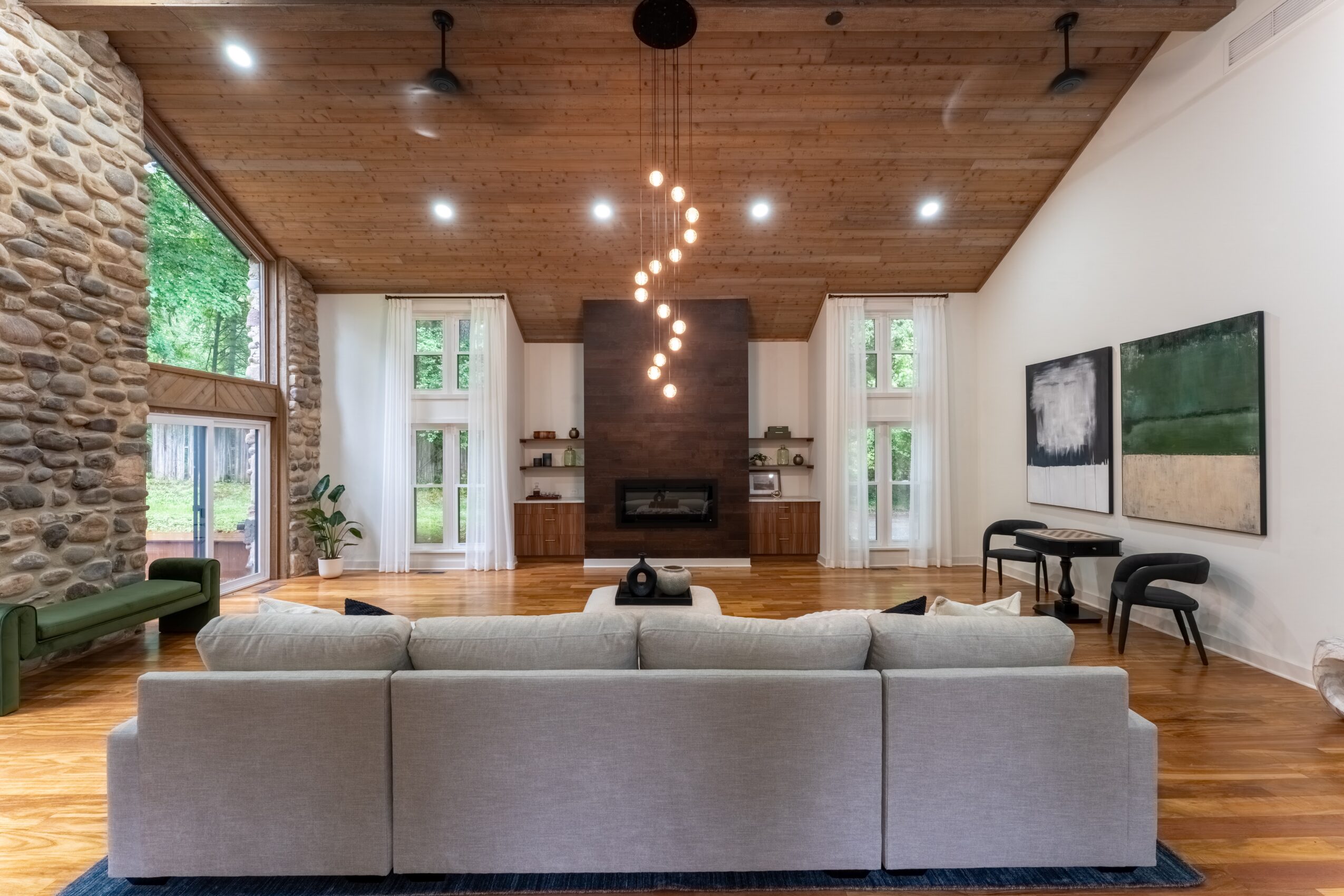 Living room with a large beige sofa, wooden ceiling, fireplace, and large windows, with artwork on the walls.
