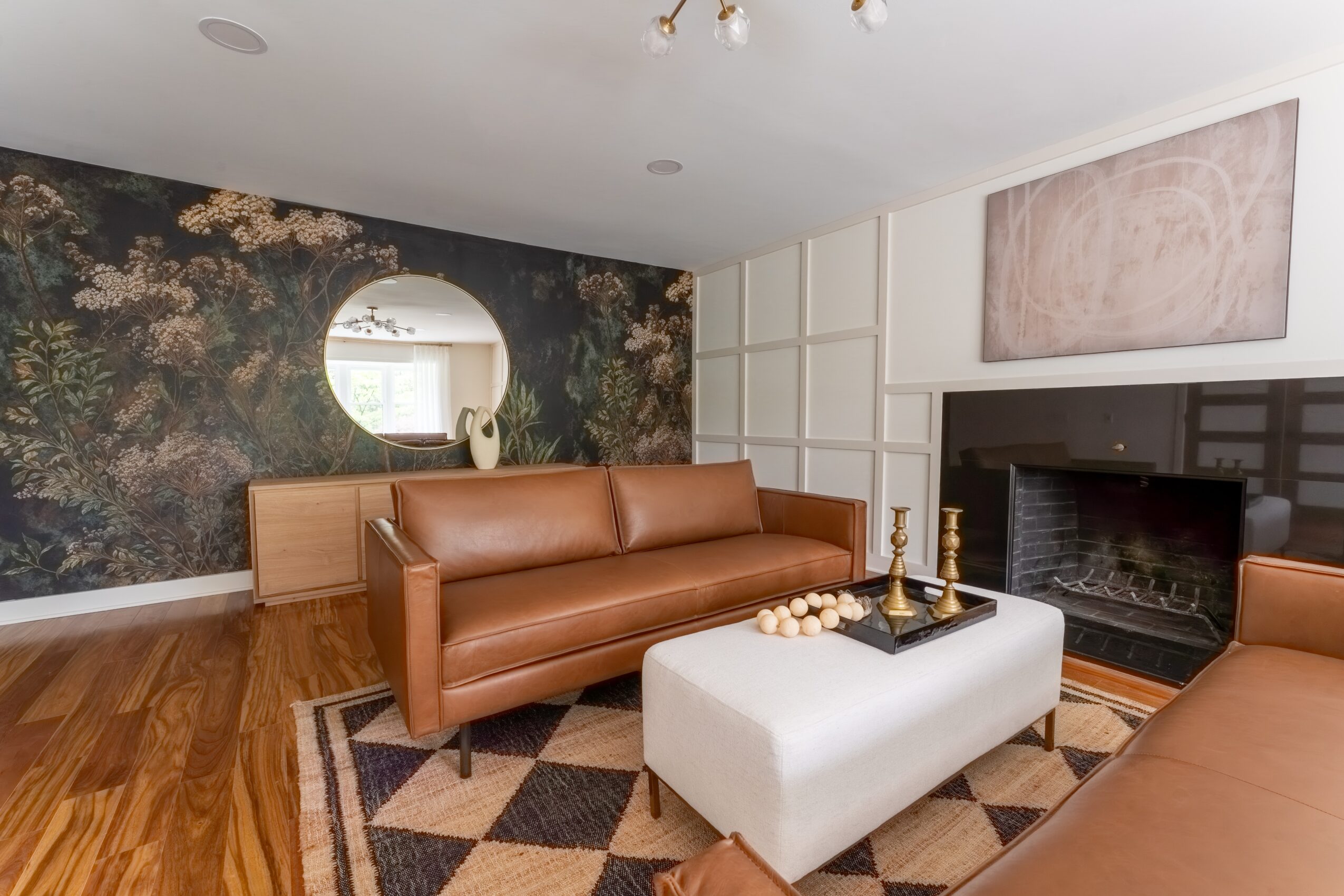 Living room with brown leather sofas, a white ottoman, a fireplace, and a patterned wall, with hardwood floors and a geometric rug.