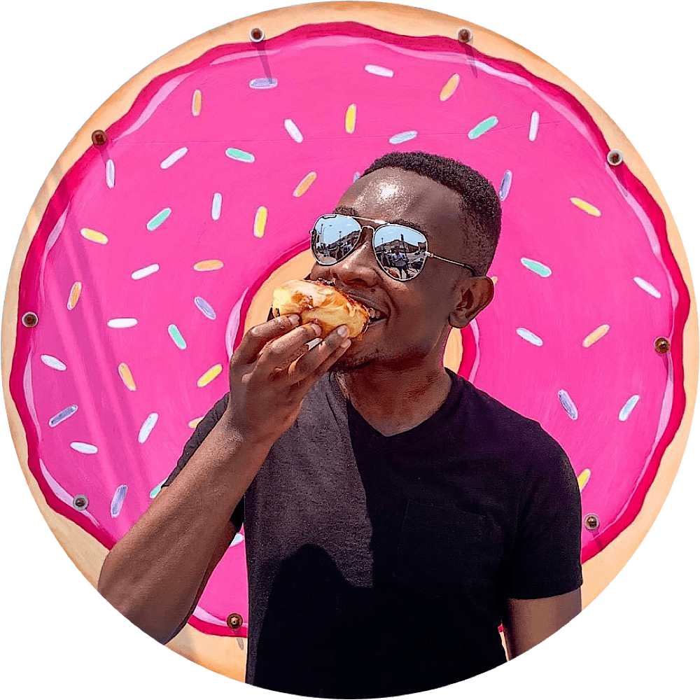 Person wearing sunglasses eating a donut in front of a pink donut-shaped background with sprinkles.