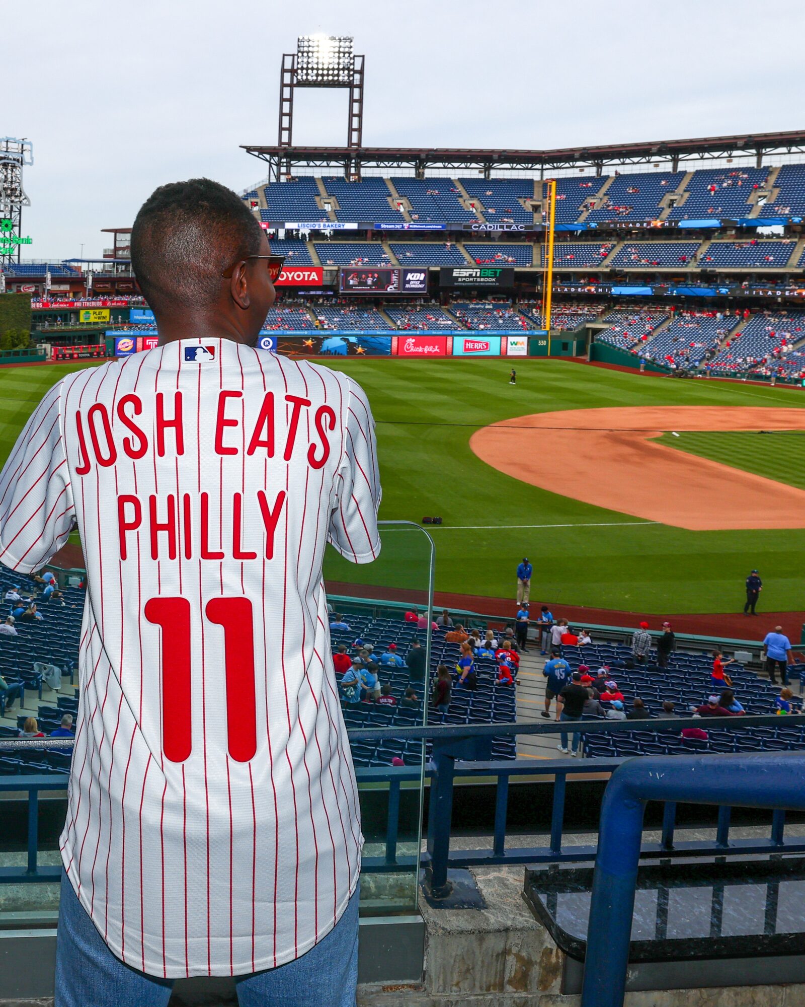 Person wearing a Phillies jersey with the name 'Josh Eats Philly' and number 11, at a baseball stadium.