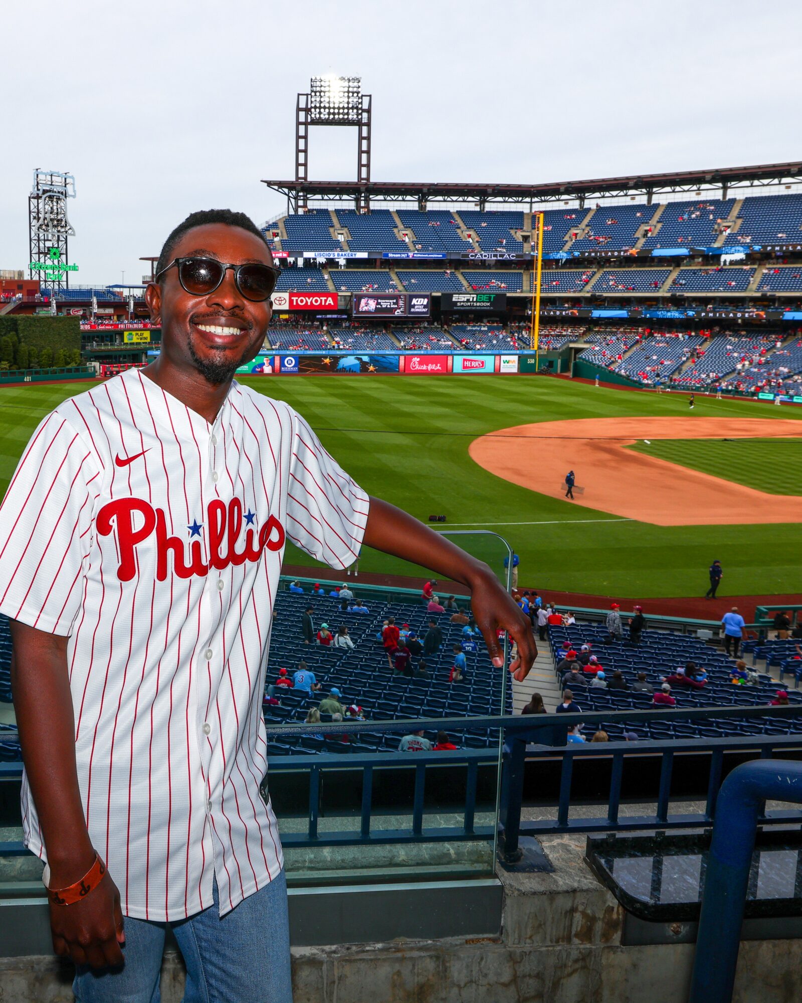 Smiling man in baseball jersey at stadium, empty seats and baseball field in background.