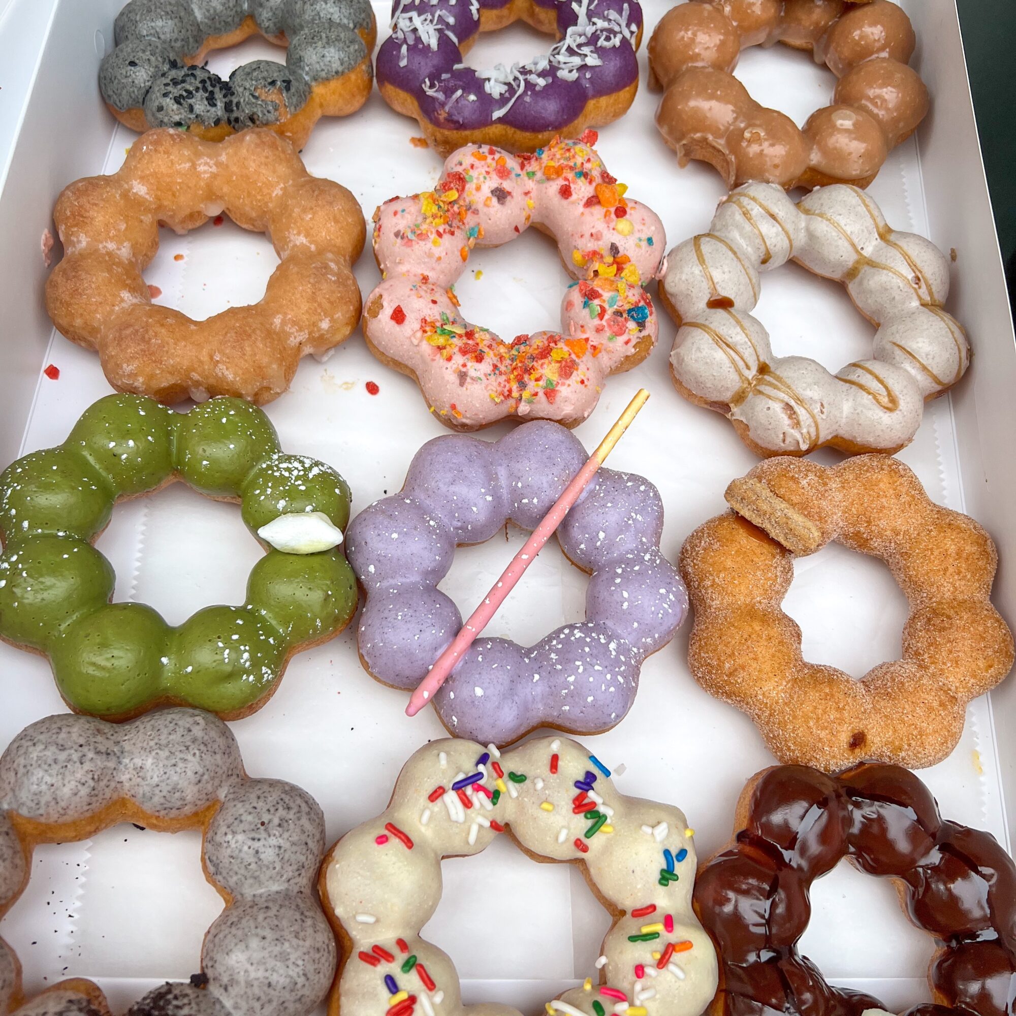 Assorted colorful donuts with various toppings arranged in a box, some with sprinkles, icing, or plain.