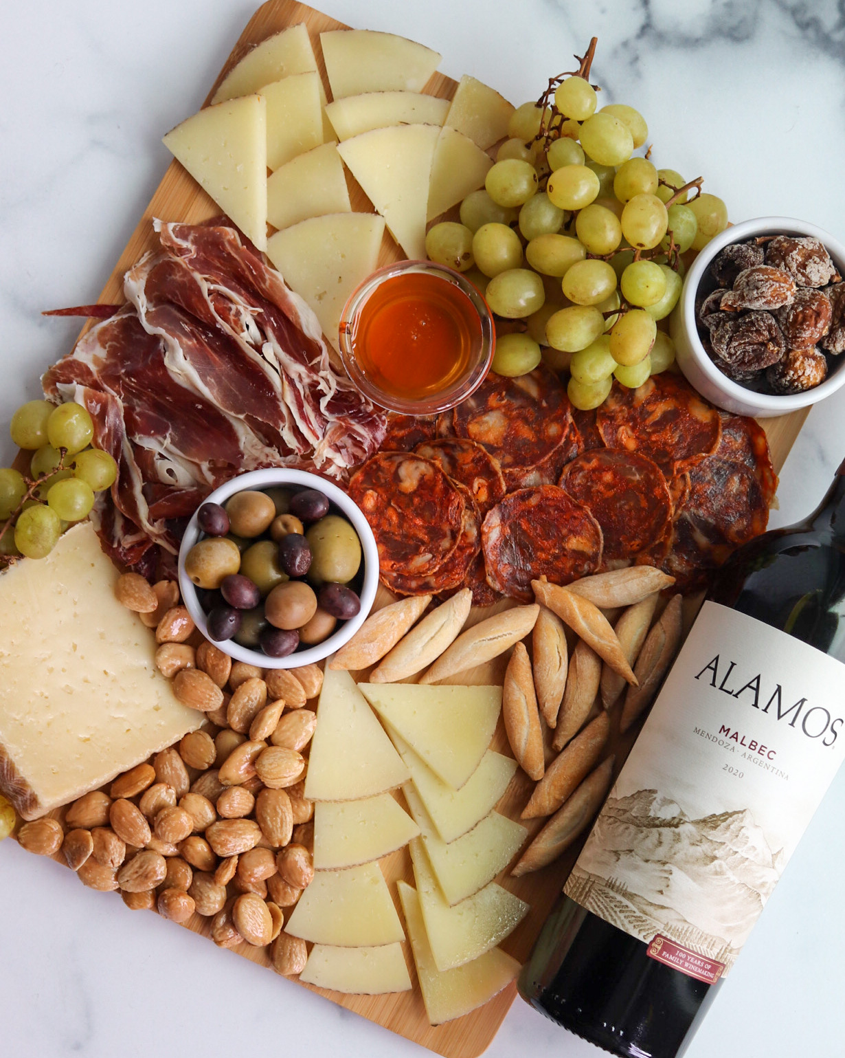 Cheese, grapes, cured meats, nuts, and a bottle of wine on a marble surface.