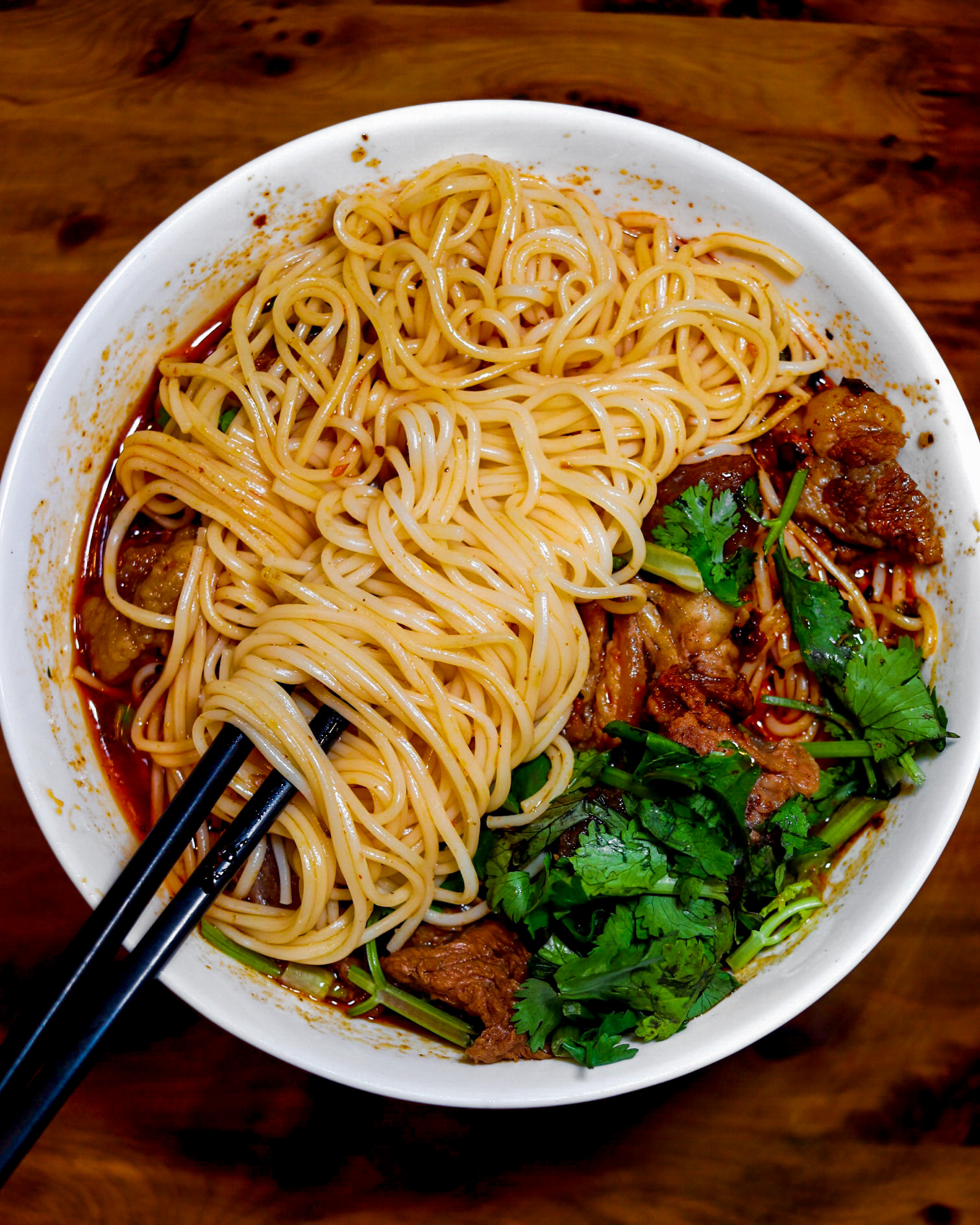 Bowl of spaghetti with meat and herbs, garnished with cilantro, on a wooden table.
