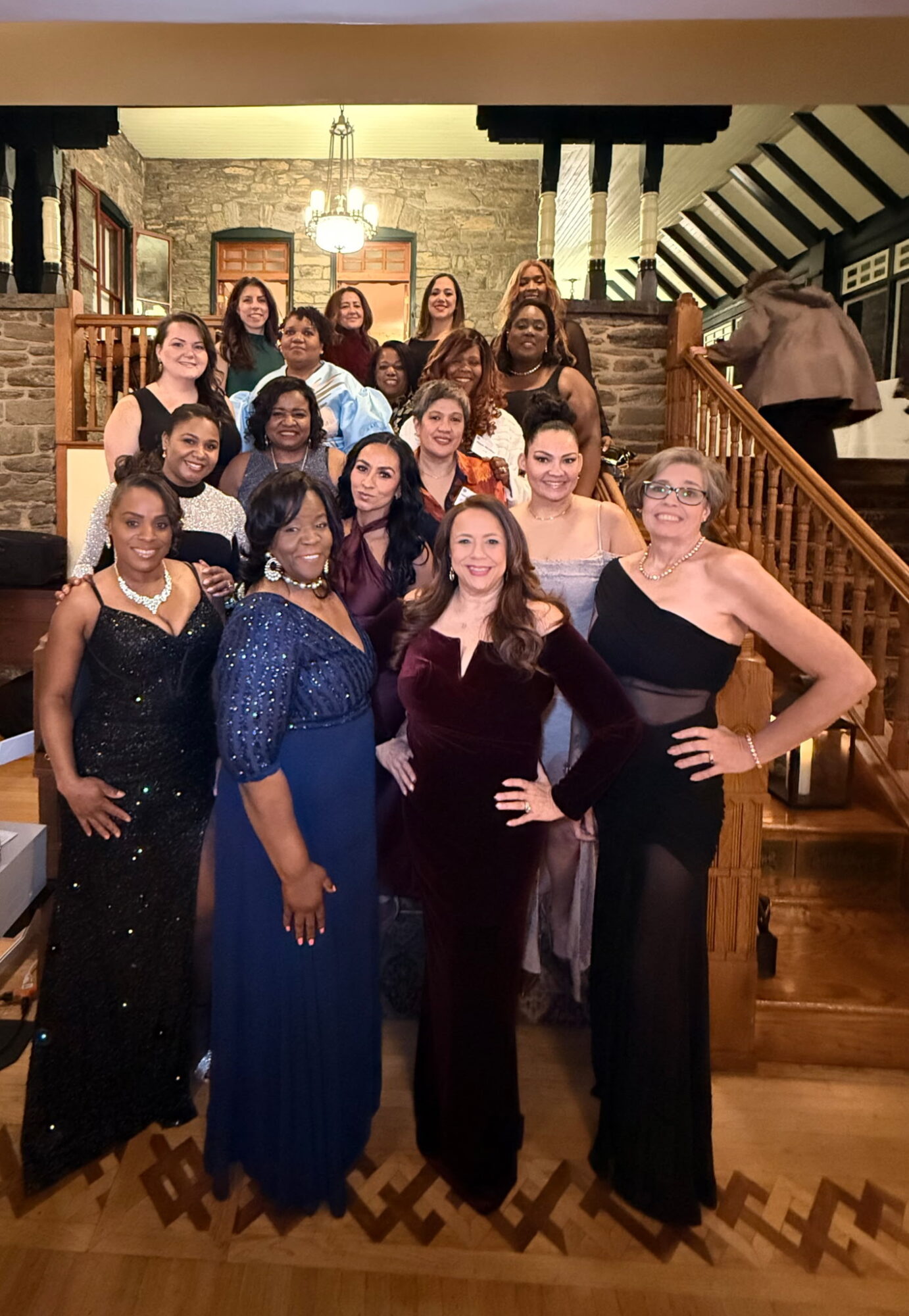Group of women in formal dresses posing on a staircase in a decorated indoor setting.