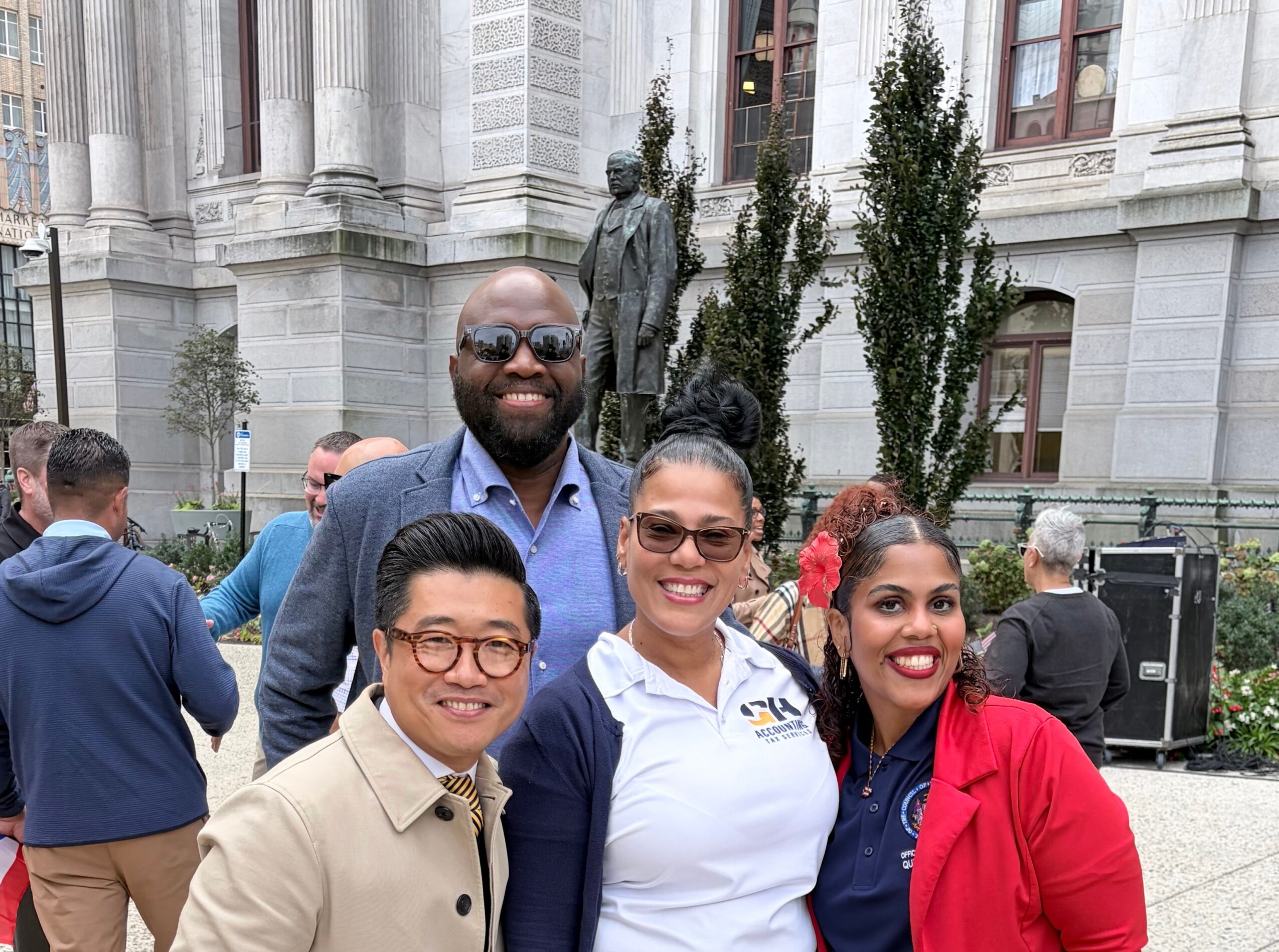 Four people smiling in front of a historic building with trees and a statue, posing for a photo.