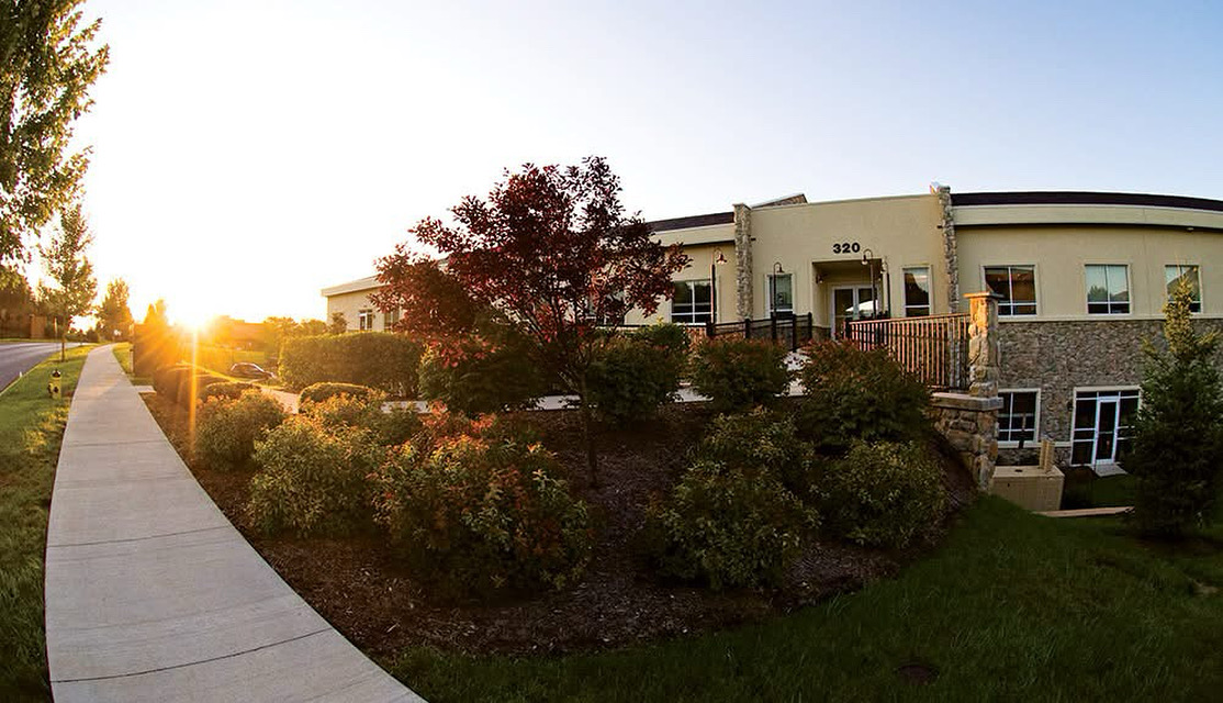 Sunset over a landscaped area with a sidewalk and a modern building in the background.