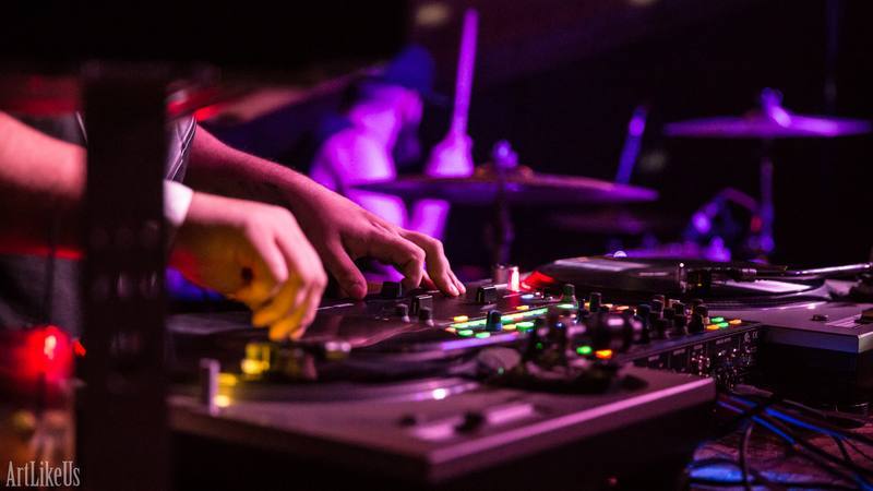 Hands operate DJ equipment with colorful lights in a dark setting.