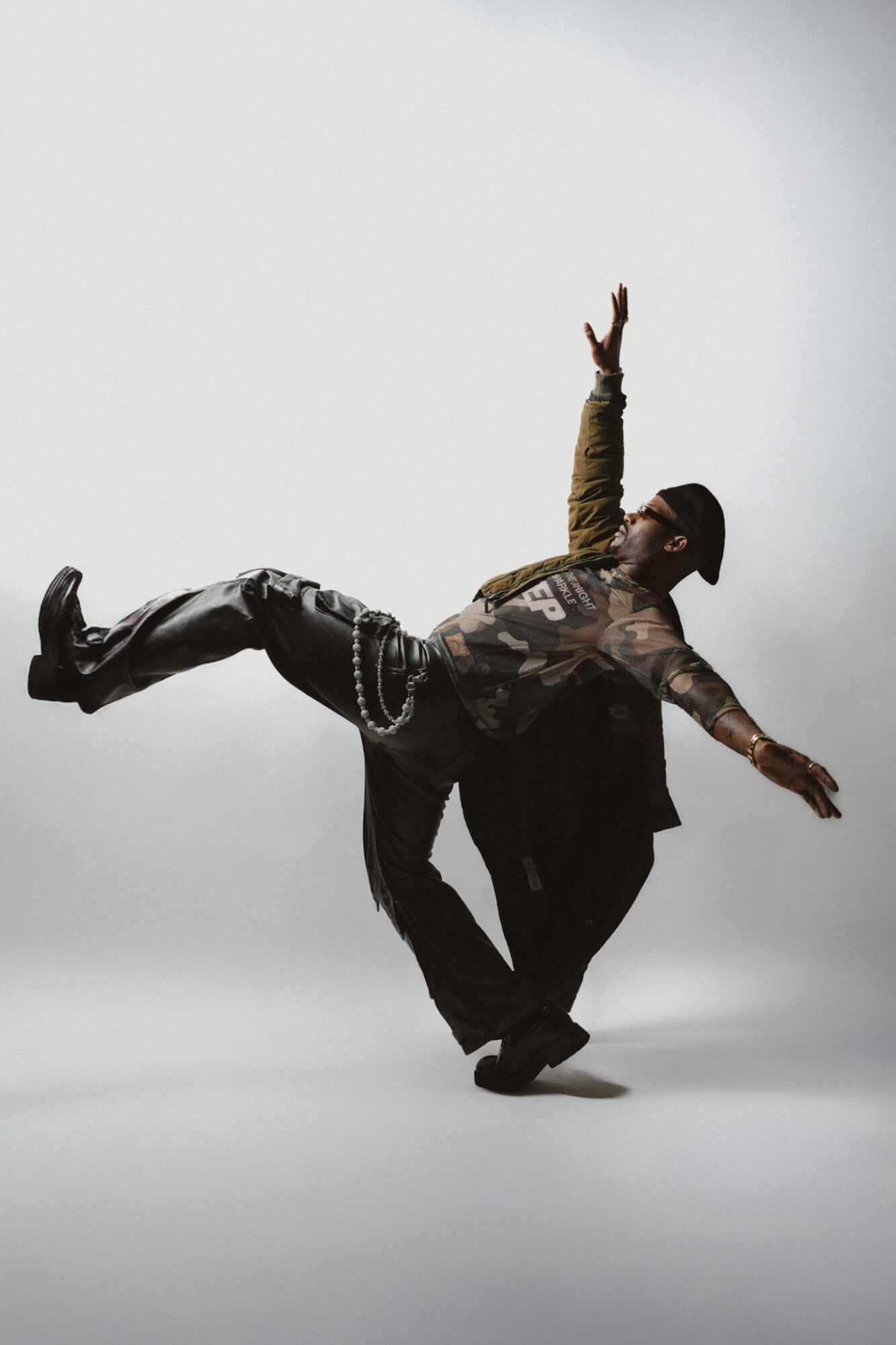 Person performing a dance move with one leg raised and arms extended, against a plain background.