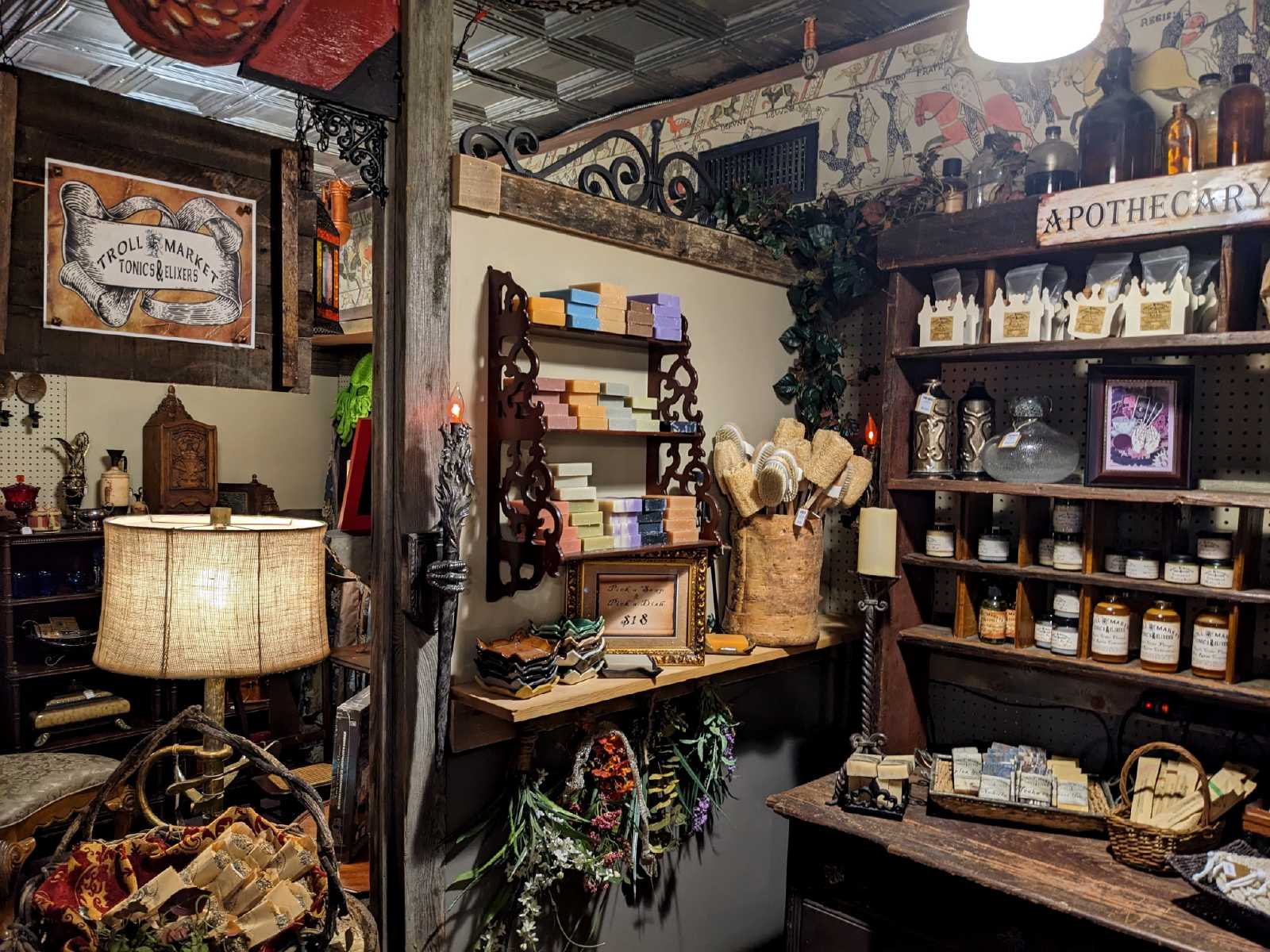 Interior of a vintage shop with shelves of jars, books, and decorative items, and a table with a telephone and other objects.