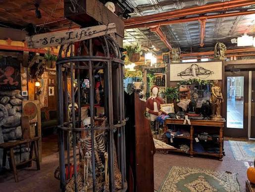 Indoor space with vintage furniture, a mannequin, and decorative items, including a cage with a skeleton and a sign reading 'S for Lifter'.