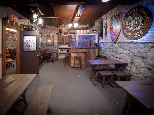 Interior of a cozy pub with wooden tables, brick walls, and decorative banners, dim lighting, and a bar area in the background.