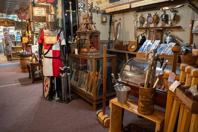 Interior of an antique shop with furniture, decorations, and a mannequin dressed in a red and white outfit.