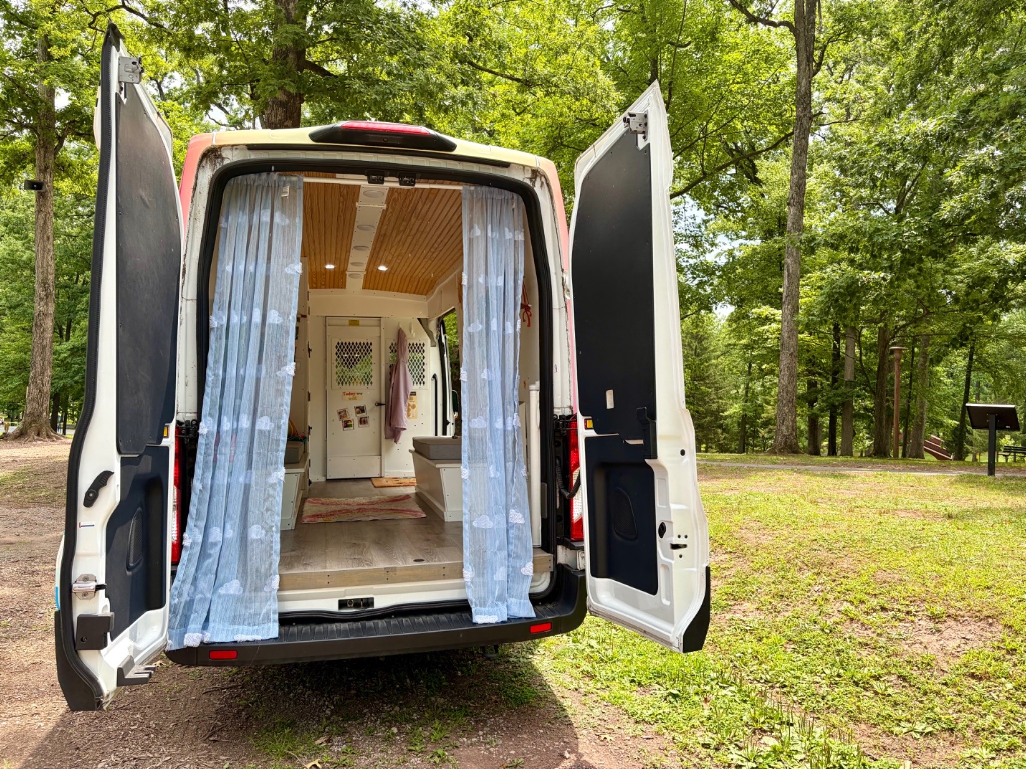 Open van with curtains inside, parked outdoors with trees and grass in background.