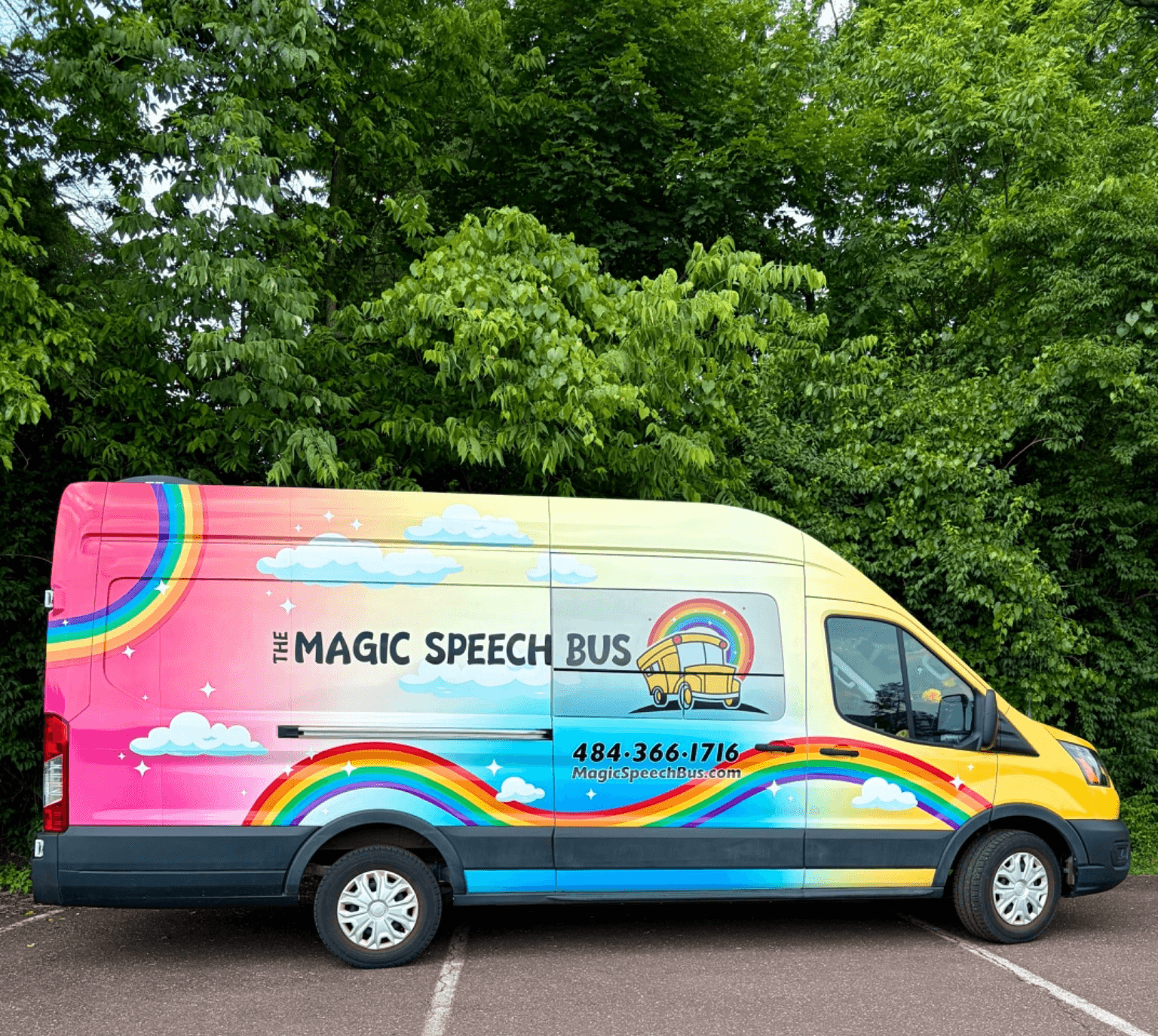 Side view of a colorful bus with rainbows and clouds, parked in front of green trees, with text and contact info.