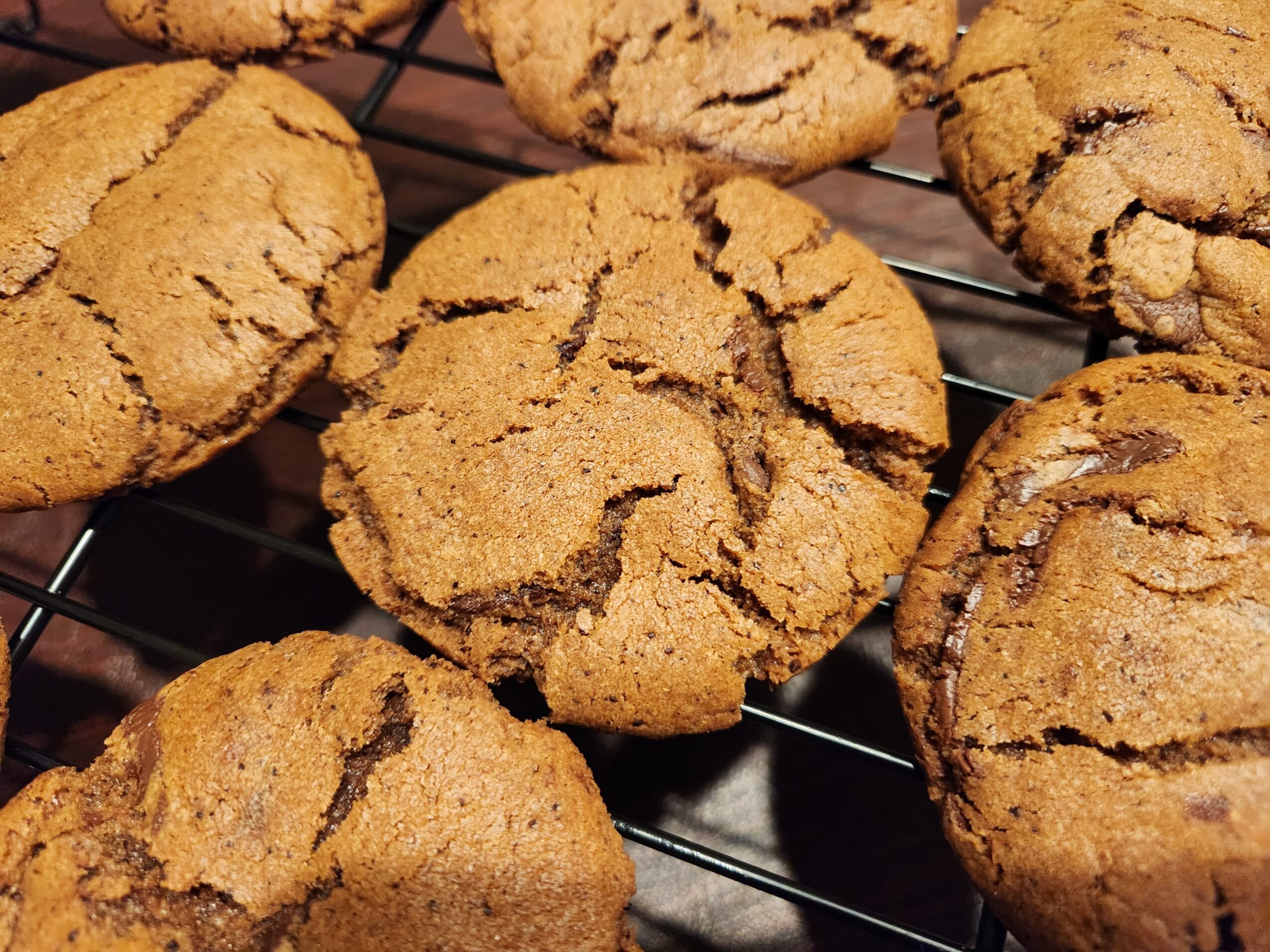 Close-up of several chocolate chip cookies on a wire rack, showing cracked surface and golden-brown color.