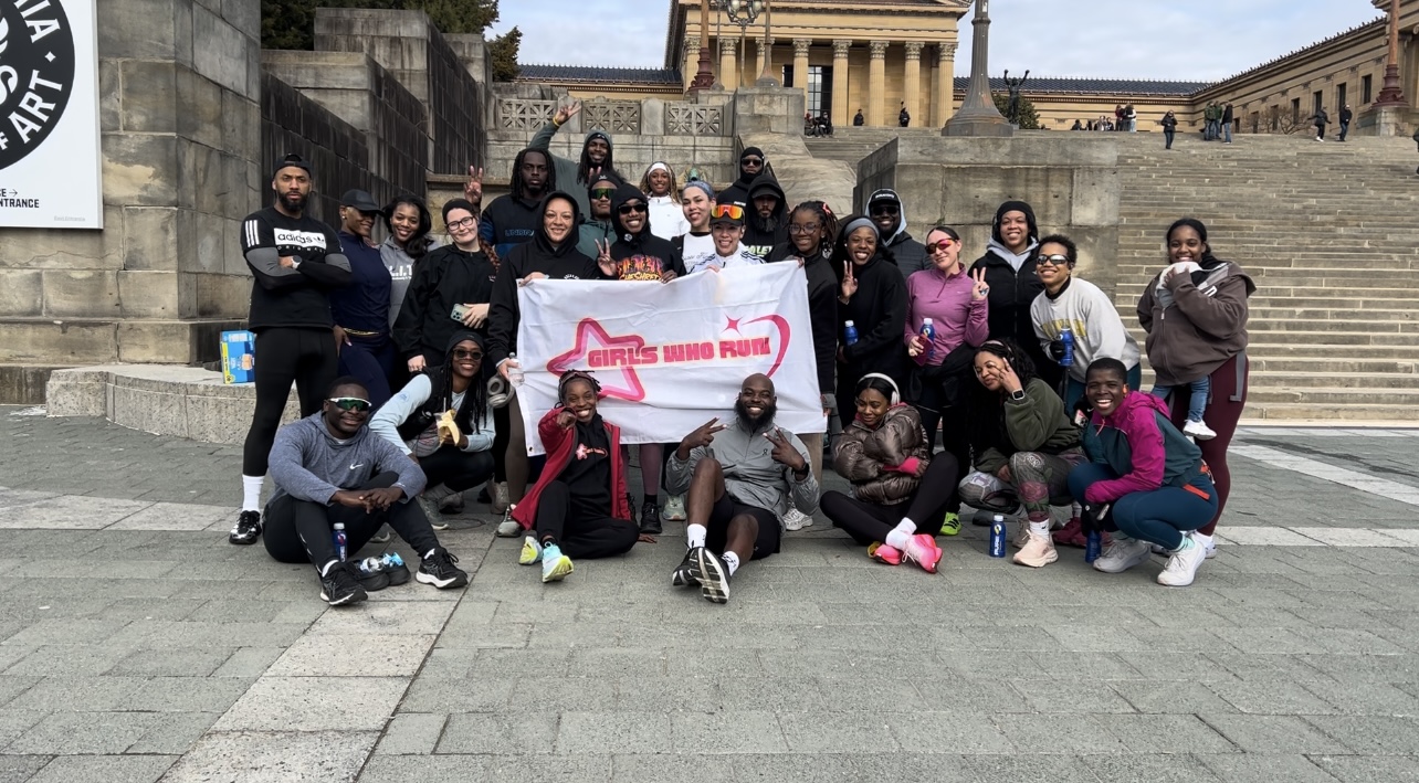 Group of people holding a banner on steps in front of a historic building, posing for a photo.