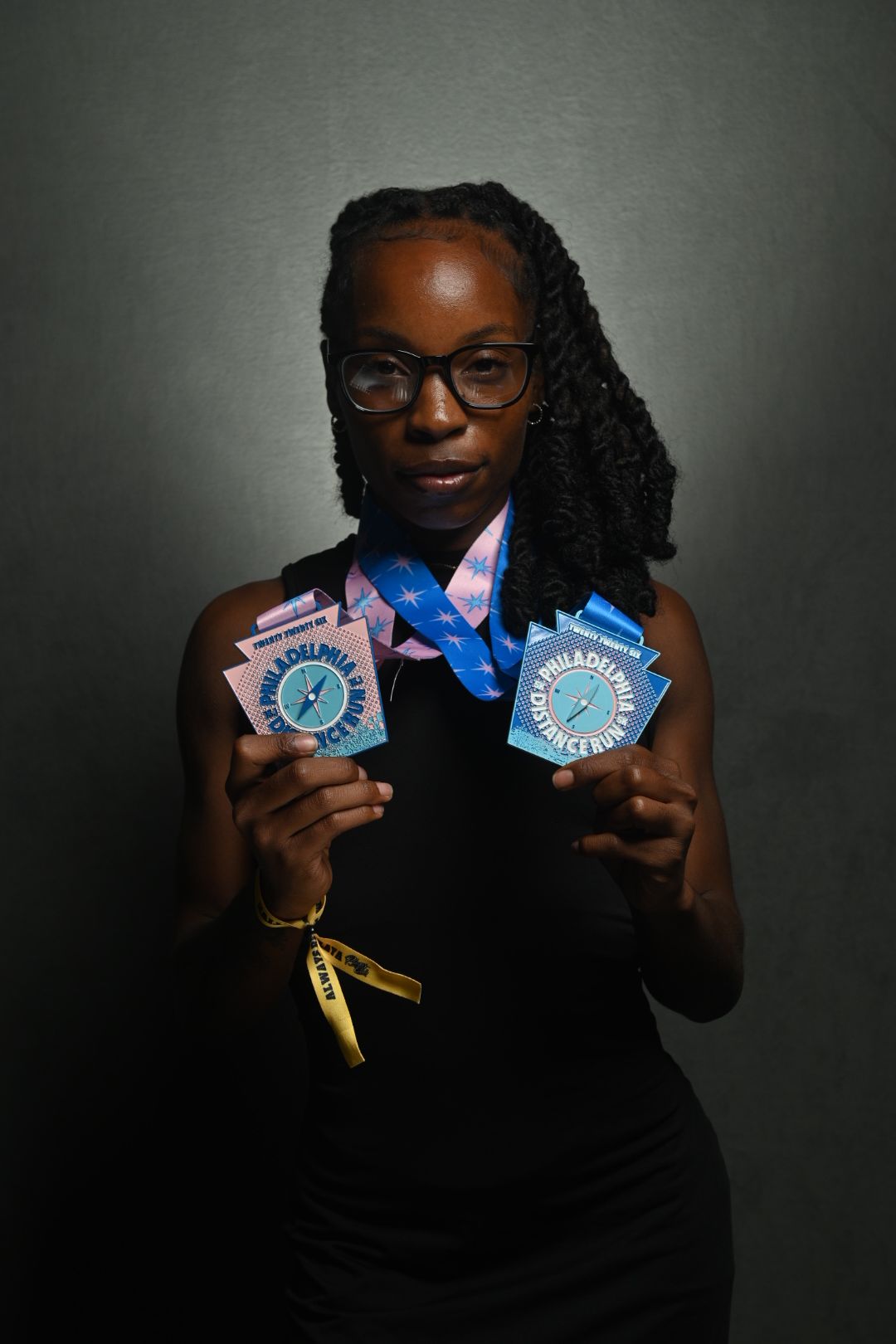 Woman with glasses holding medals, smiling, against a plain background.