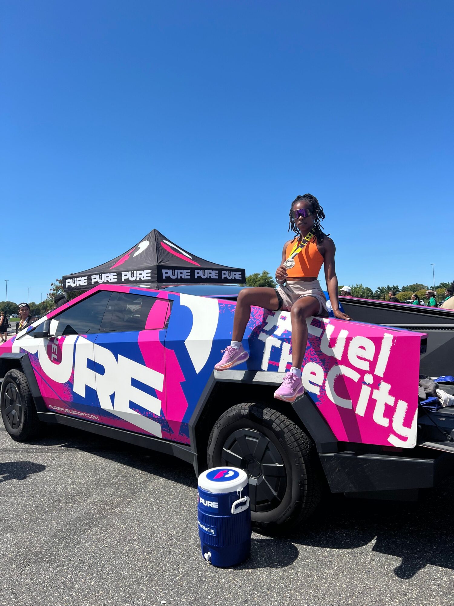Person standing on a vehicle with colorful branding, holding a drink, under a clear blue sky.