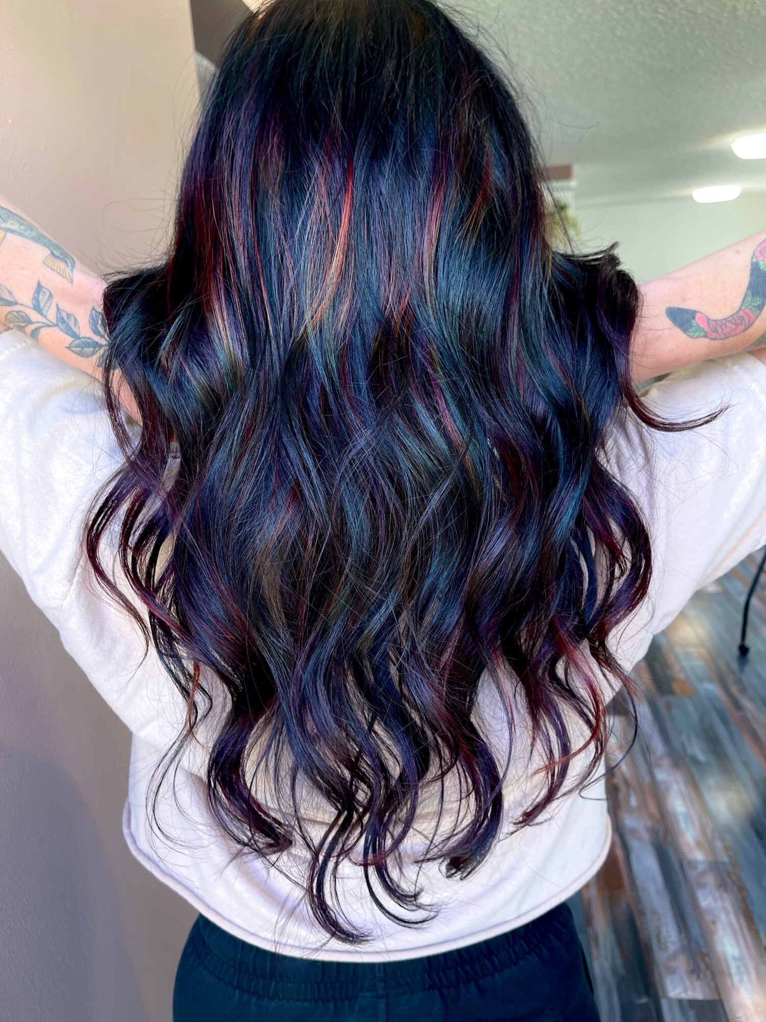 Person with long, wavy hair dyed in shades of blue, purple, and pink, seen from the back.