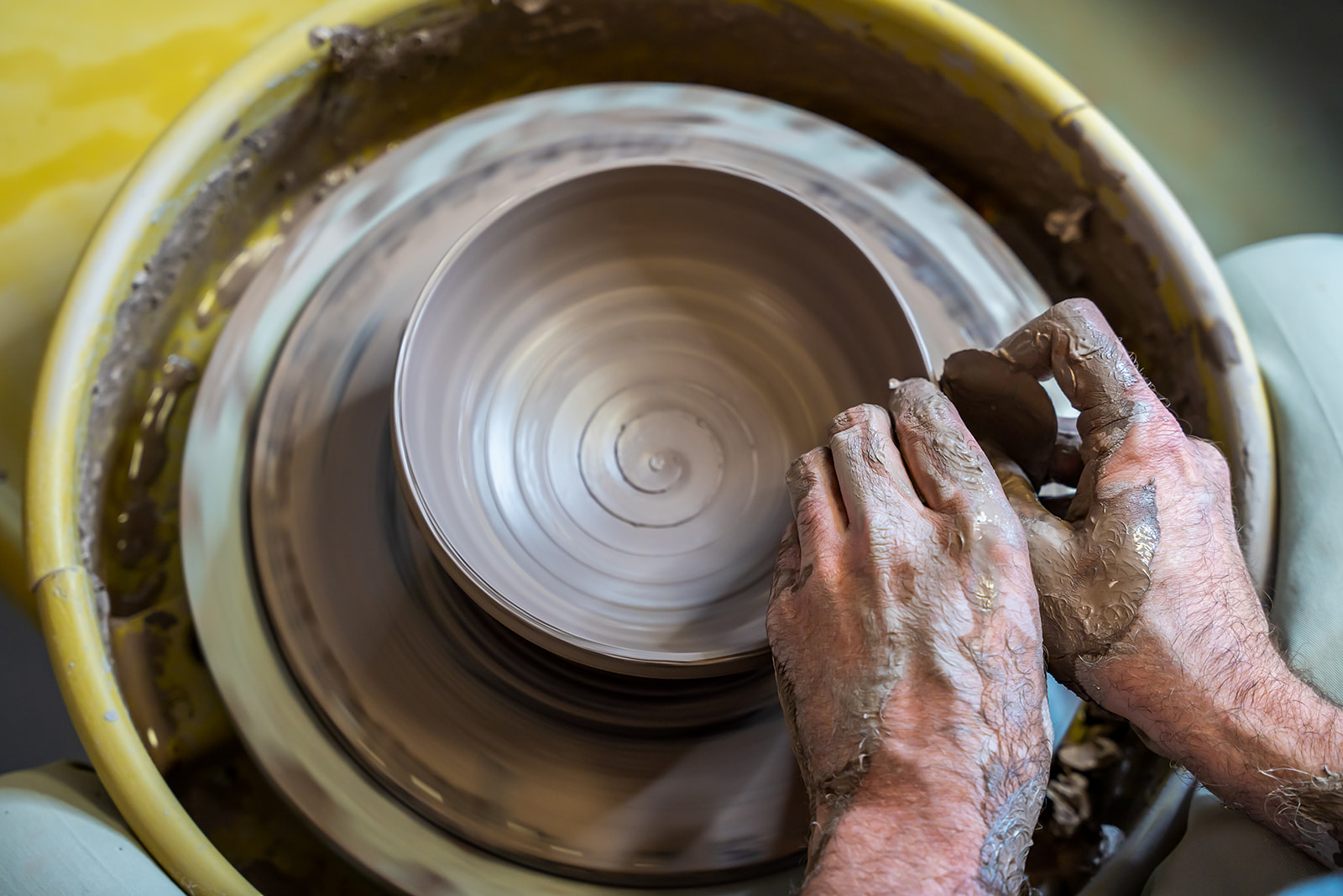 Hands shaping clay on a spinning pottery wheel, with wet clay on hands and wheel surface.