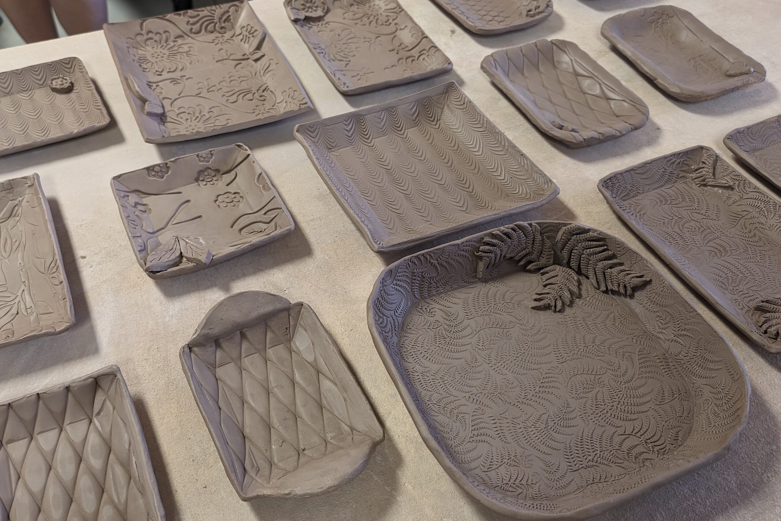 Various textured and patterned ceramic plates and trays arranged on a table, some with geometric or abstract designs.