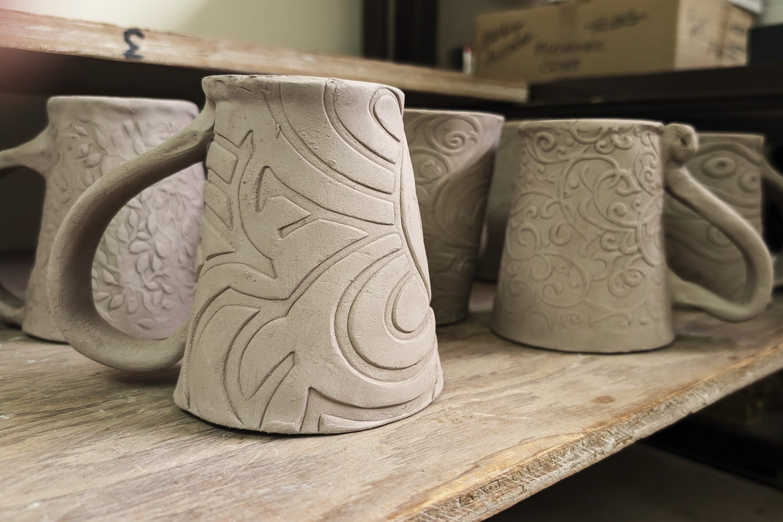 Four ceramic mugs with textured patterns on a wooden surface, some with handles, in a row.