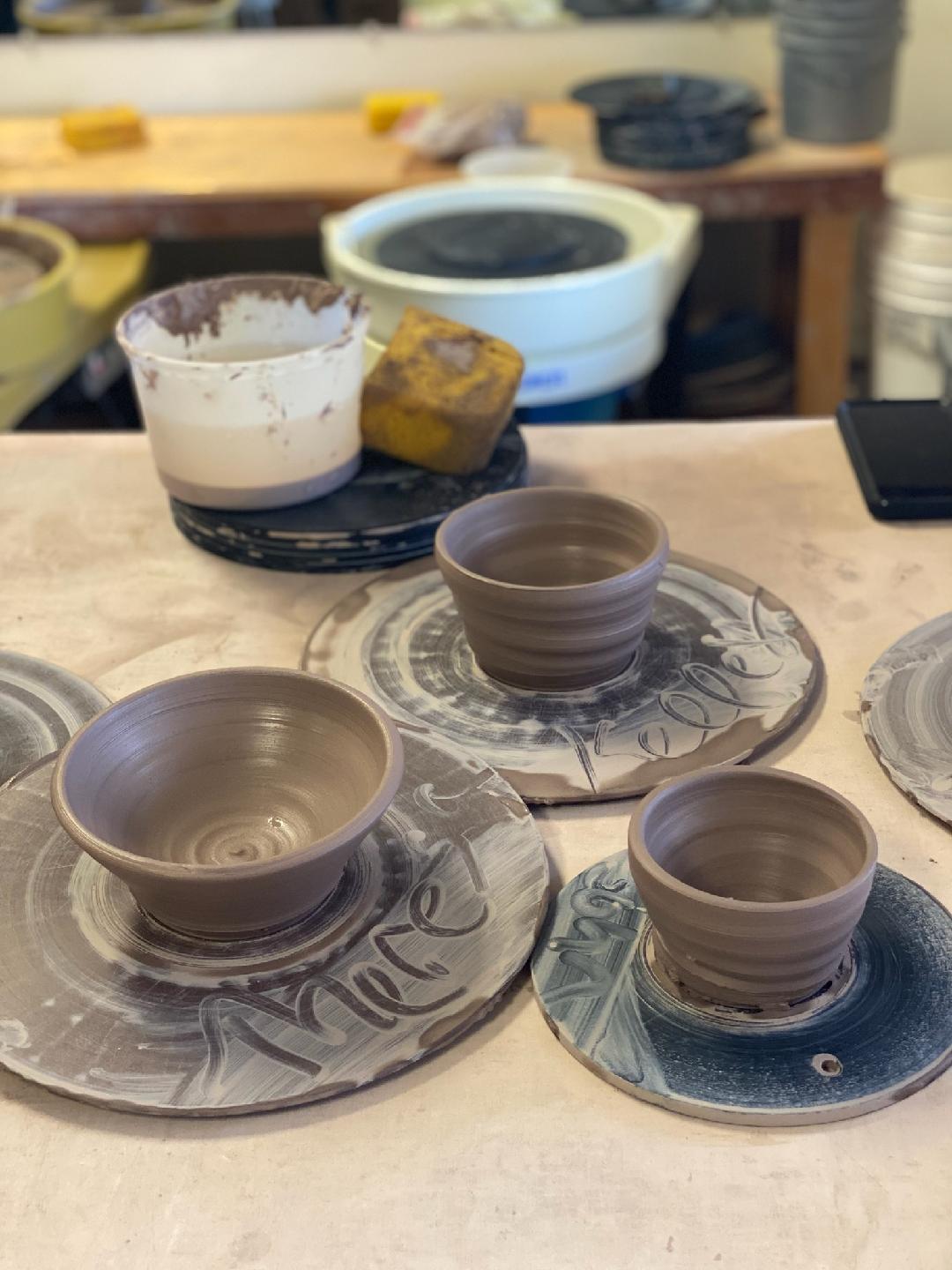 Three ceramic bowls on decorative plates with a pottery wheel and tools in the background.