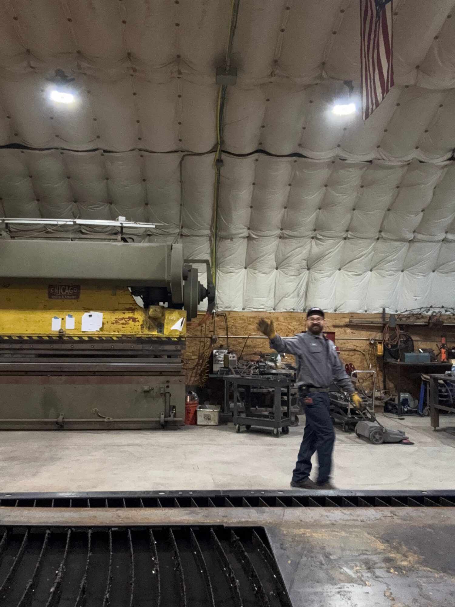 Person standing near equipment in a workshop with a padded ceiling, tools, and machinery visible.