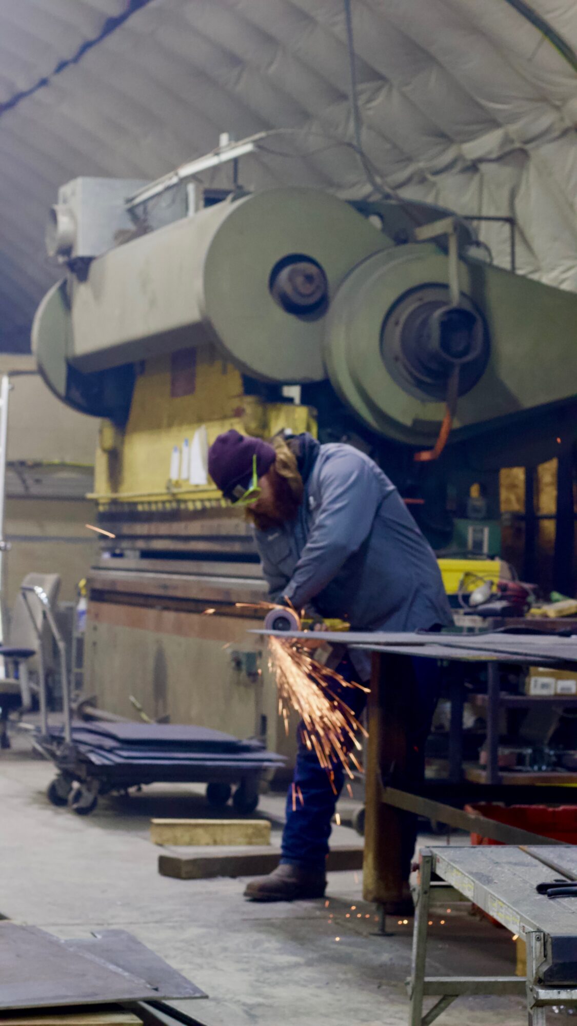 Person working with sparks flying in an industrial workshop with large machinery overhead.